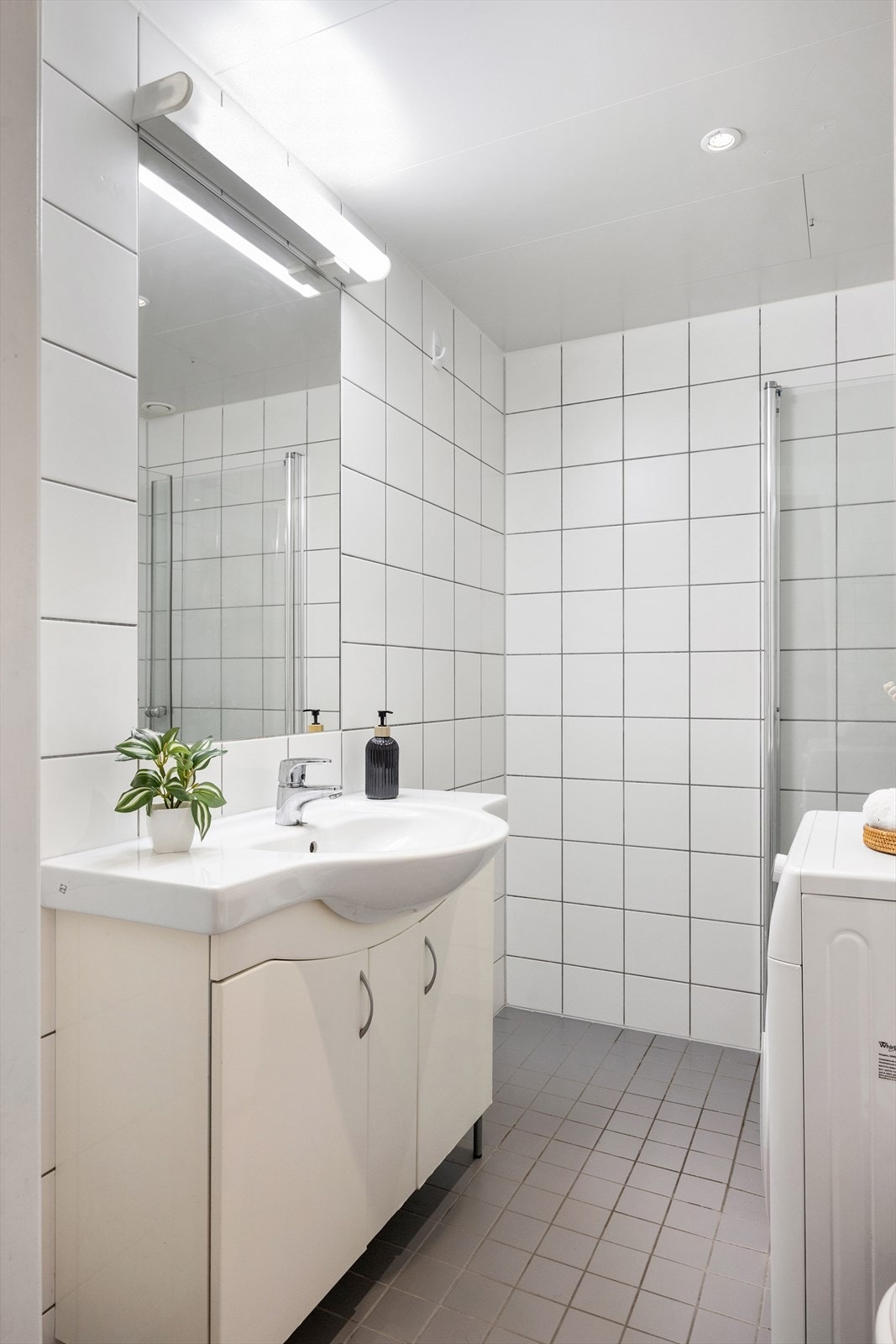 Badet har servantskap med nedfelt servant, innebygd speil med lys, vegghengt toalett med innebygd sisterne, og dusjsone med innfelte dusjdører i herdet glass. Galleribilde