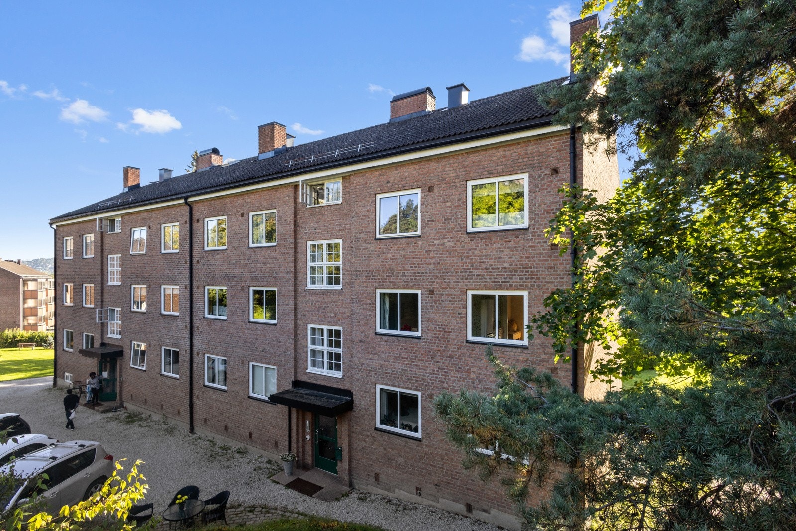 Fasaden mot Hotvetveien. Det er noen parkeringsplasser i gårdsplassen. Ut over disse er det gateparkering. Galleribilde