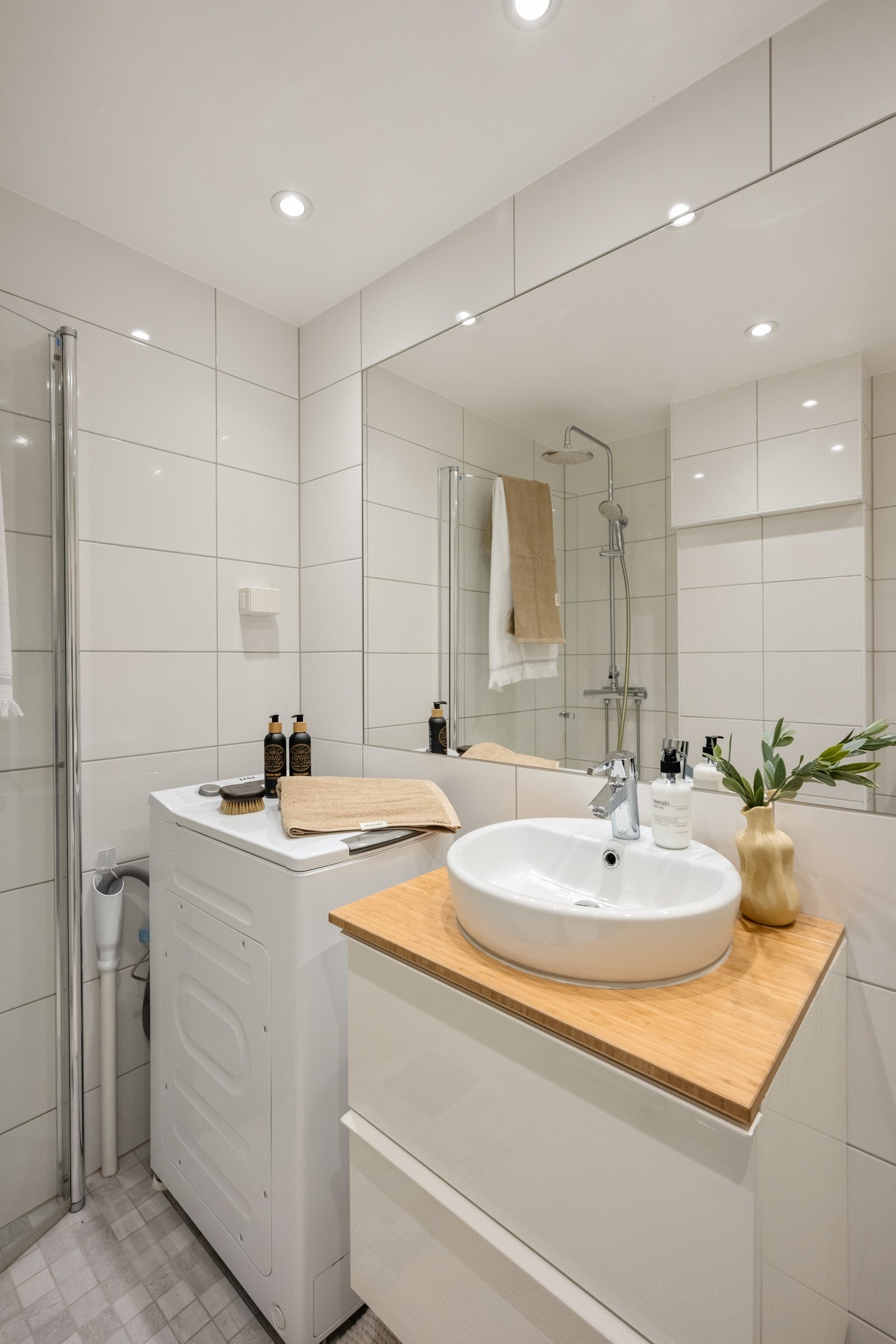 Badet er utstyrt med dusj på gulv med dører i herdet glass, klosett og servant. Galleribilde