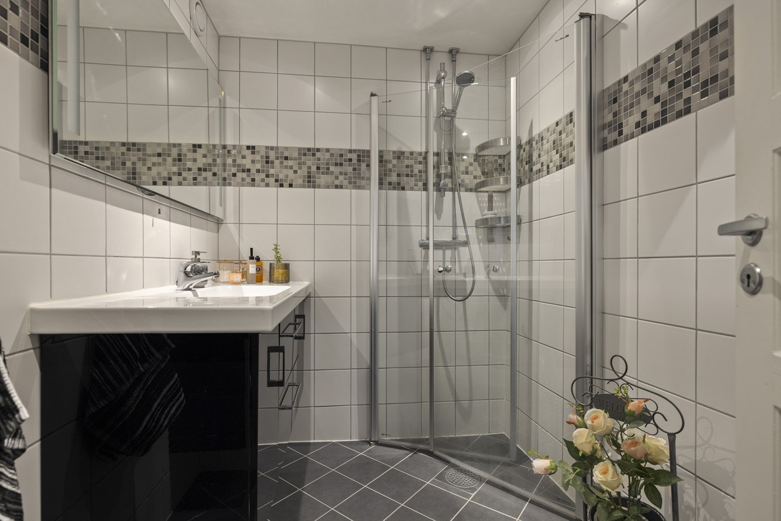 Pent flislagt bad fra 2016 med downlights og varmekabler. Sort høyglans innredning med slette fronter med ovenpåliggende servant i helstøpt plate. Dusjen er utstyrt med veggmonterte dusjdører i herdet glass og et stilrent dusjamatur. Galleribilde