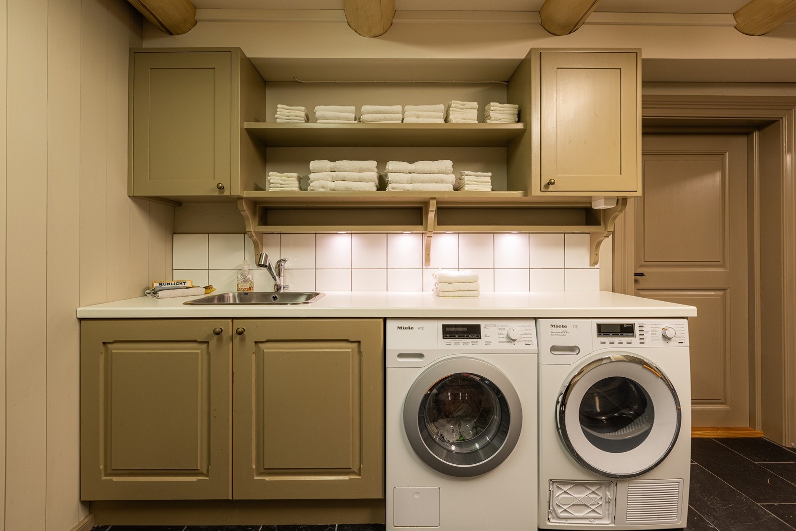 Vaskerommet har flislagt skifergulv med vannbåren gulvvarme. Rommet er utstyrt med opplegg for vaskemaskin og tørketrommel. Galleribilde