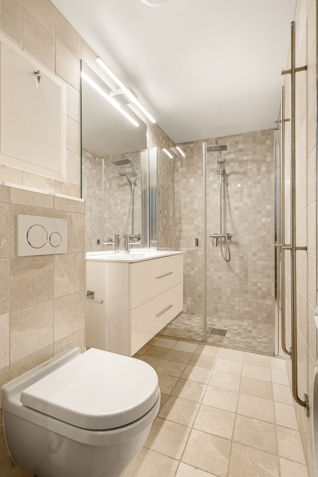 Moderne bad fra 2017 med flislagte overflater, samt elektrisk gulvvarme for ekstra komfort. Innerst i rommet finner man en dusjnisje med dusjdør, regnfallsdusj og håndholdt spylefunksjon. Galleribilde