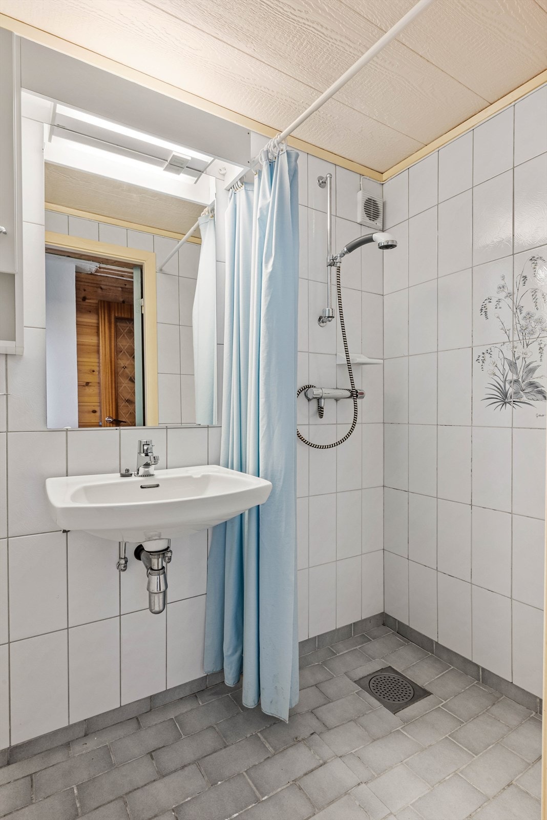 Kjellerbadet er flislagt og har åpen dusj, veggmontert servant, speil og lysarmatur med stikk. Galleribilde