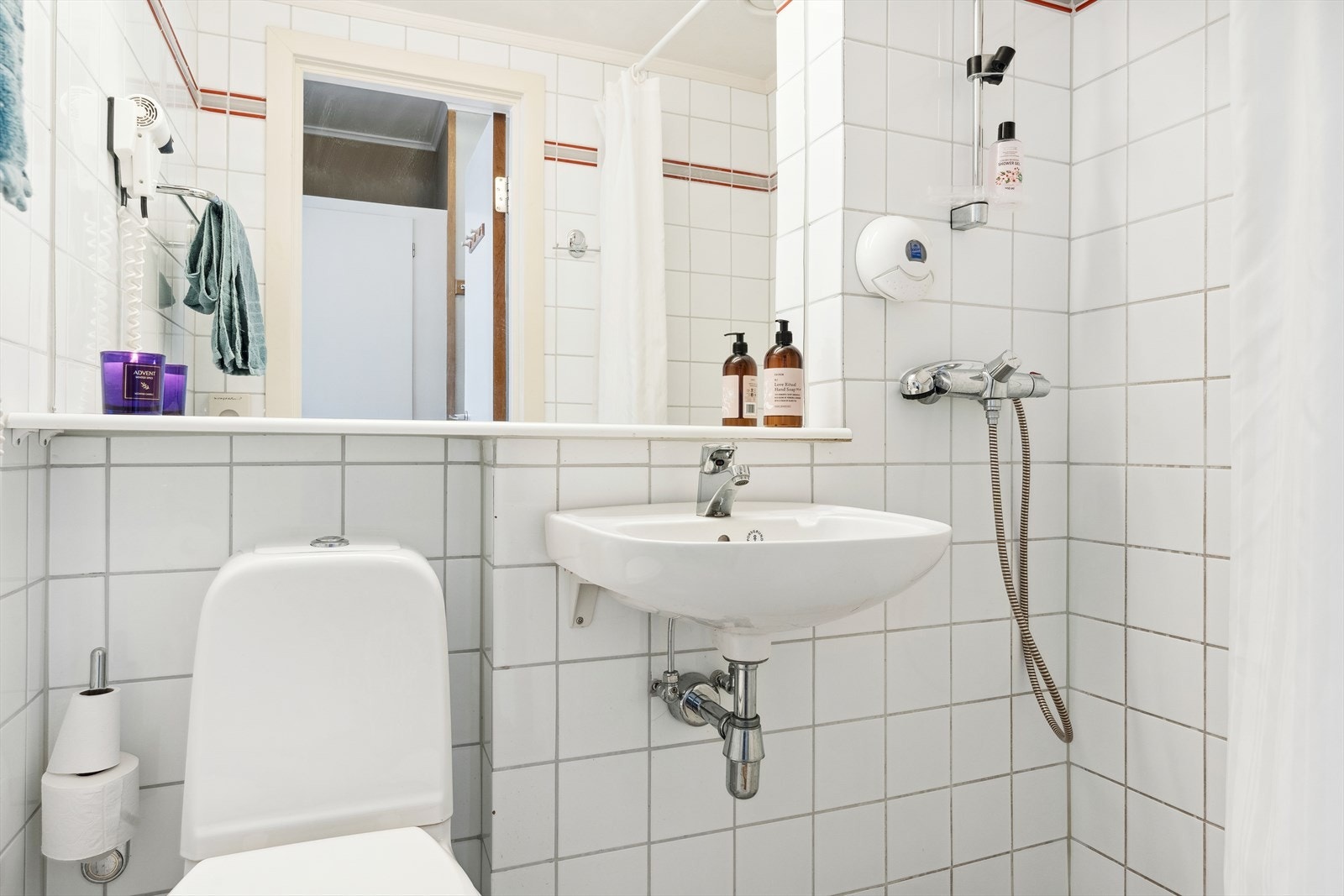 Bad 1 med flisbelagt overflater med varmekabler i gulv. Montert vegghengt porselenservant, gulvstående toalett, vegghengt speil og åpen dusj i hjørne. Galleribilde