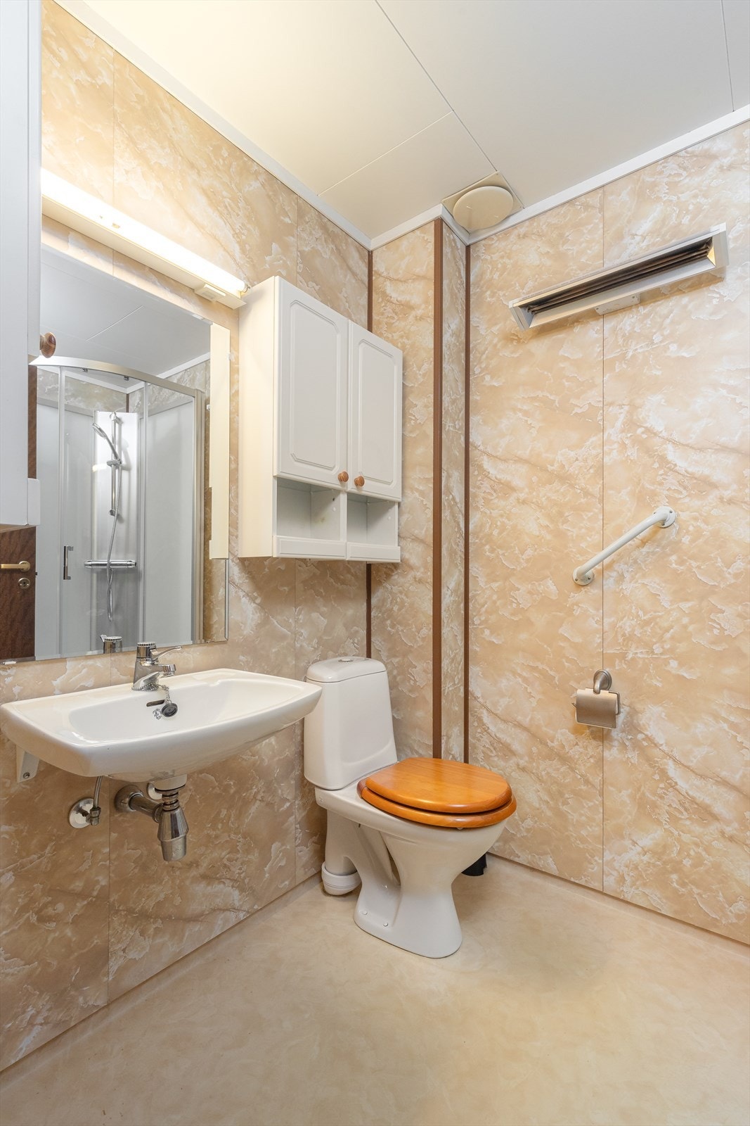 Rommet er utstyrt med vegghengt servant med speilflate og belysning over vask samt vegghengte skaper på siden med hvite, profilerte fronter. Galleribilde