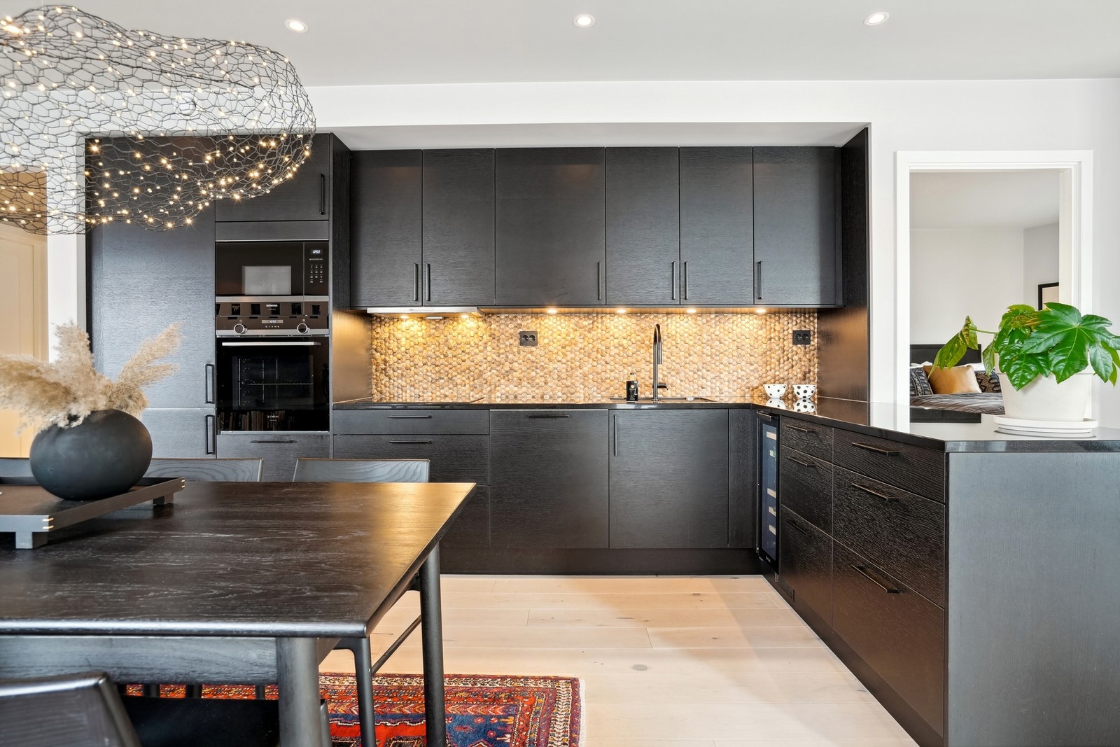 Stilrent kjøkken med innredning i "Trapes Sort Eik" fra Norema, kombinert med en eksklusiv benkeplate i Nero Assoluto 3 cm granitt fra Gautvik Steinindustri. Høykvalitets integrerte hvitevarer gir en elegant finish. Galleribilde