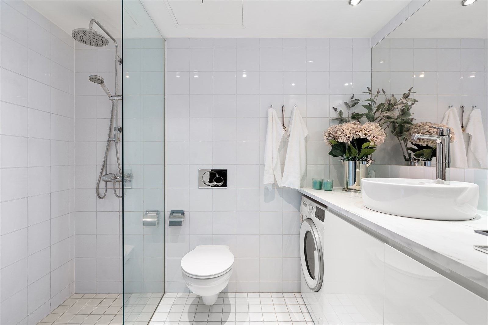 Lyst og pent baderom med dusjnisje, vegghengt toalett og baderomsmøbel med plass til vaskemaskin. Galleribilde