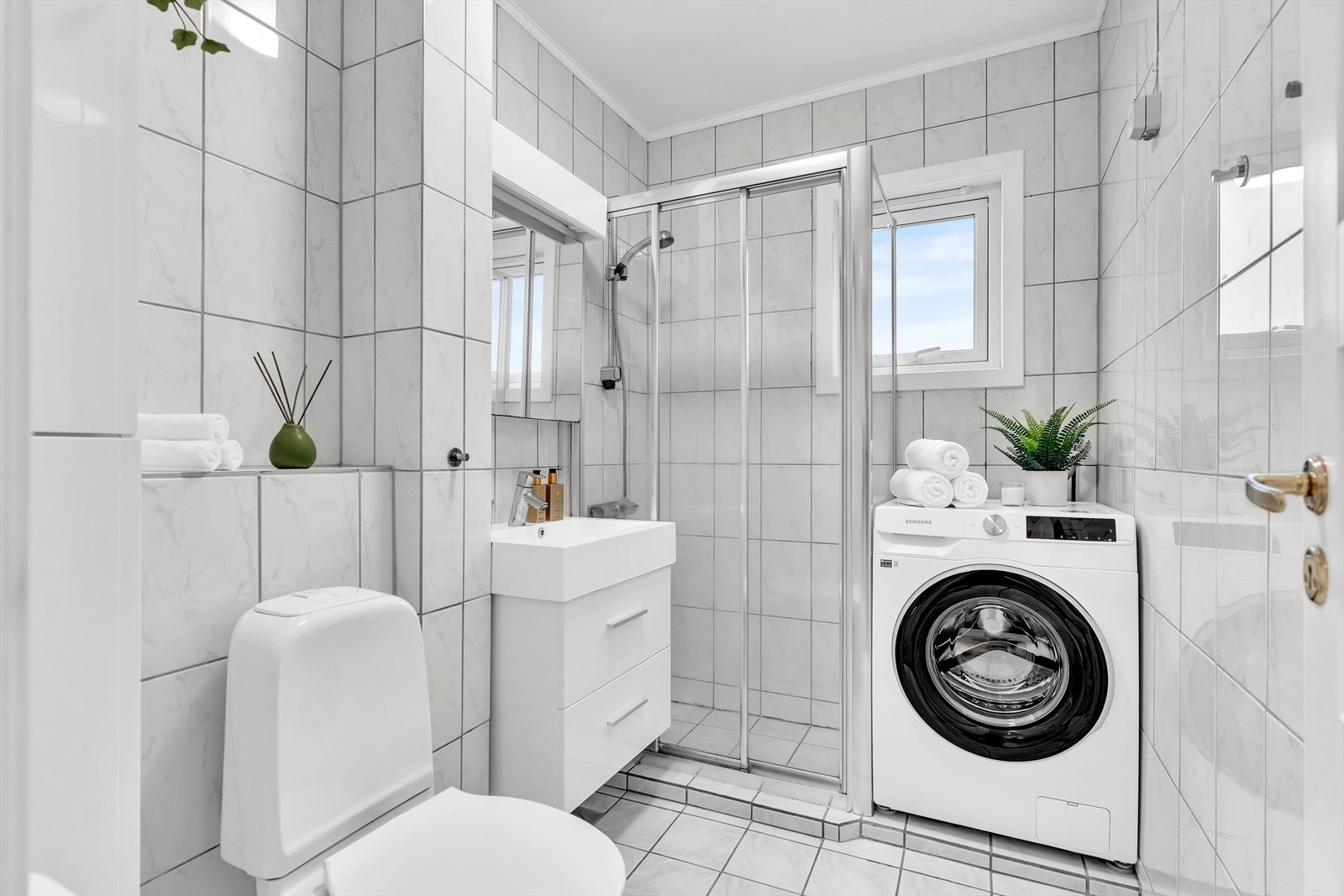 Lyst og flislagt bad med opplegg for vaskemaskin. Galleribilde