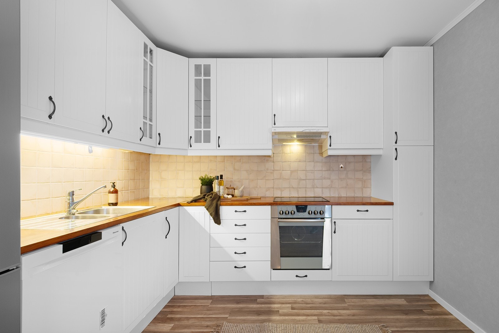 Innredningen har over- og underskap i en funksjonell L-form, med profilerte fronter, heltre benkeplate og fliser på vegg over benk. Hvitevarer medfølger. Galleribilde