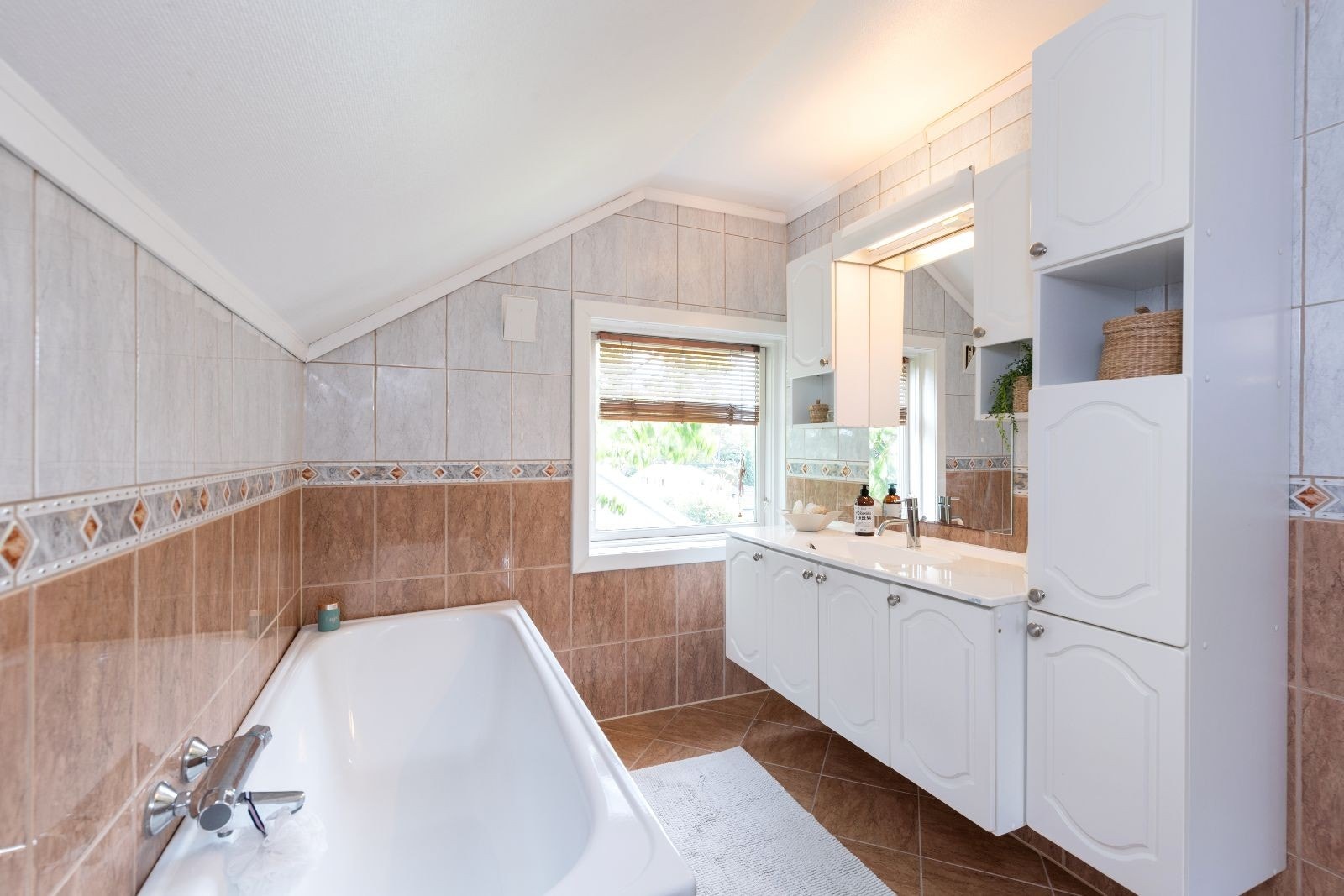 Bad med fliser på gulv og vegger. Badekar, wc og servant med innredning Galleribilde