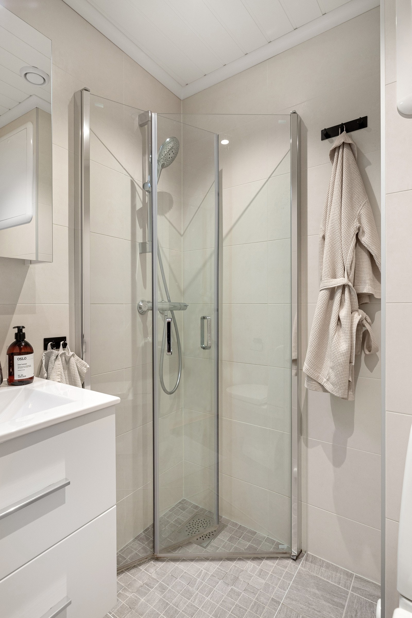 Svingbar dusjvegg og termostatstyrt dusjbatteri i krom med hånddusj. Veggmontert speilskap med belysning og servantskap med heldekkende vask. Galleribilde