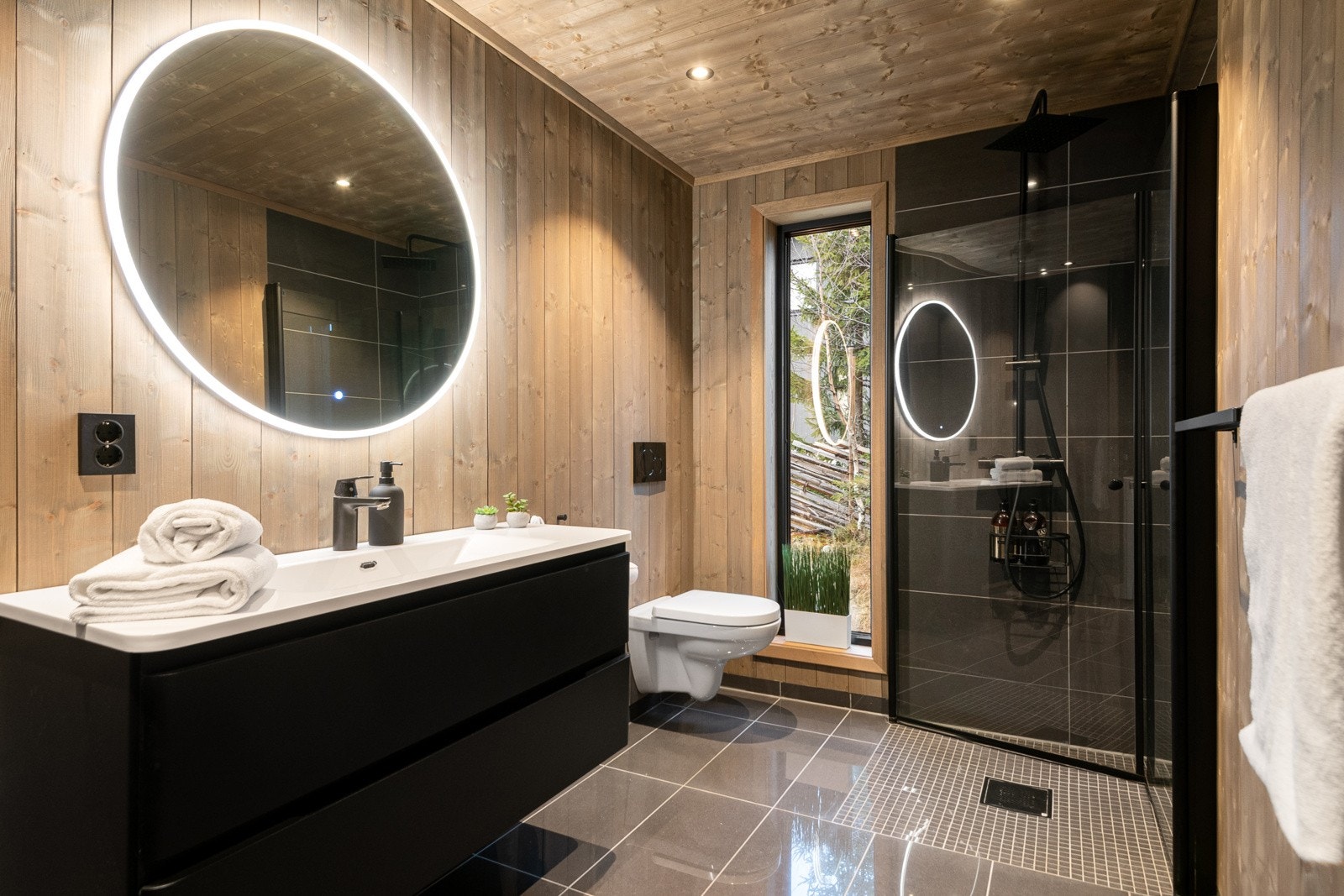 Hovedbadet har inngang fra entréen og er av svært generøs størrelse. Her finnes igjen et stort baderomsmøbel med servant og speil med lys, vegghengt toalett og dusjnisje med både regndusj og vanlig dusjhode. Galleribilde