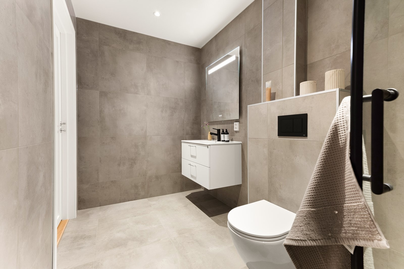 Baderomsinnredning fra Drømmekjøkkenet med speil, heldekkende servant og armatur i krom utførelse. Vegghengt toaøett og dusjhjørne med innfellbare glassdører. Galleribilde