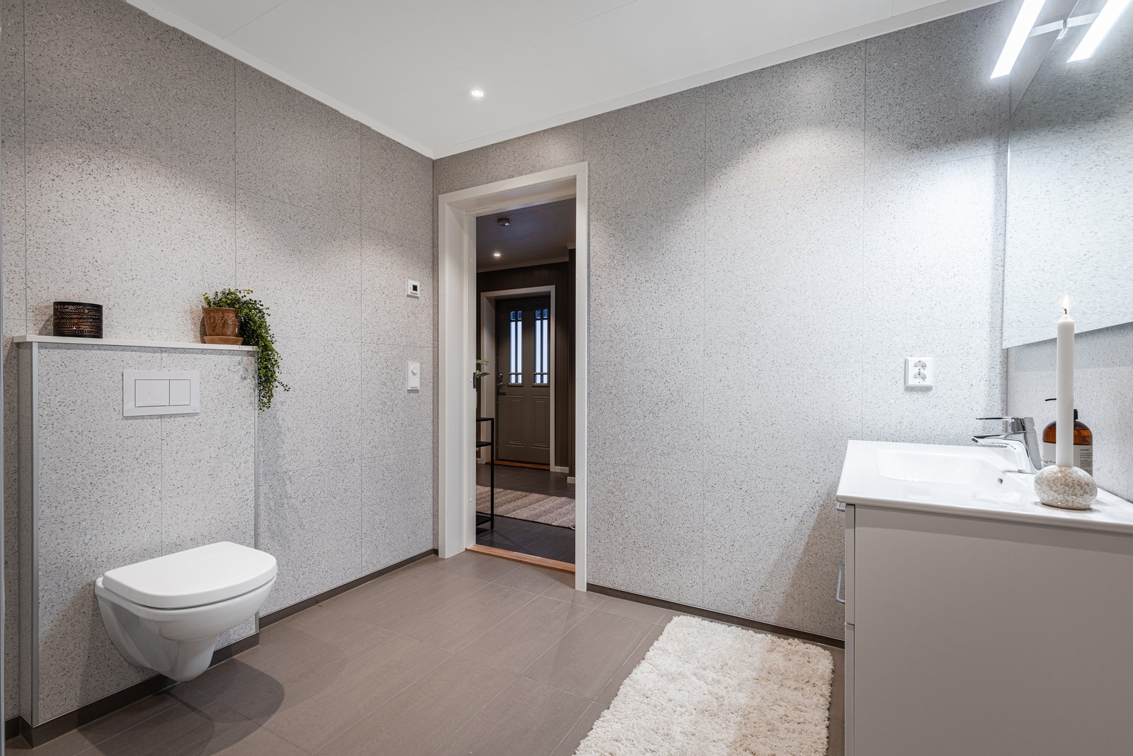 Med dusjhjørne, vegghengt toalett og baderomsinnredning med speil og overlys. Galleribilde