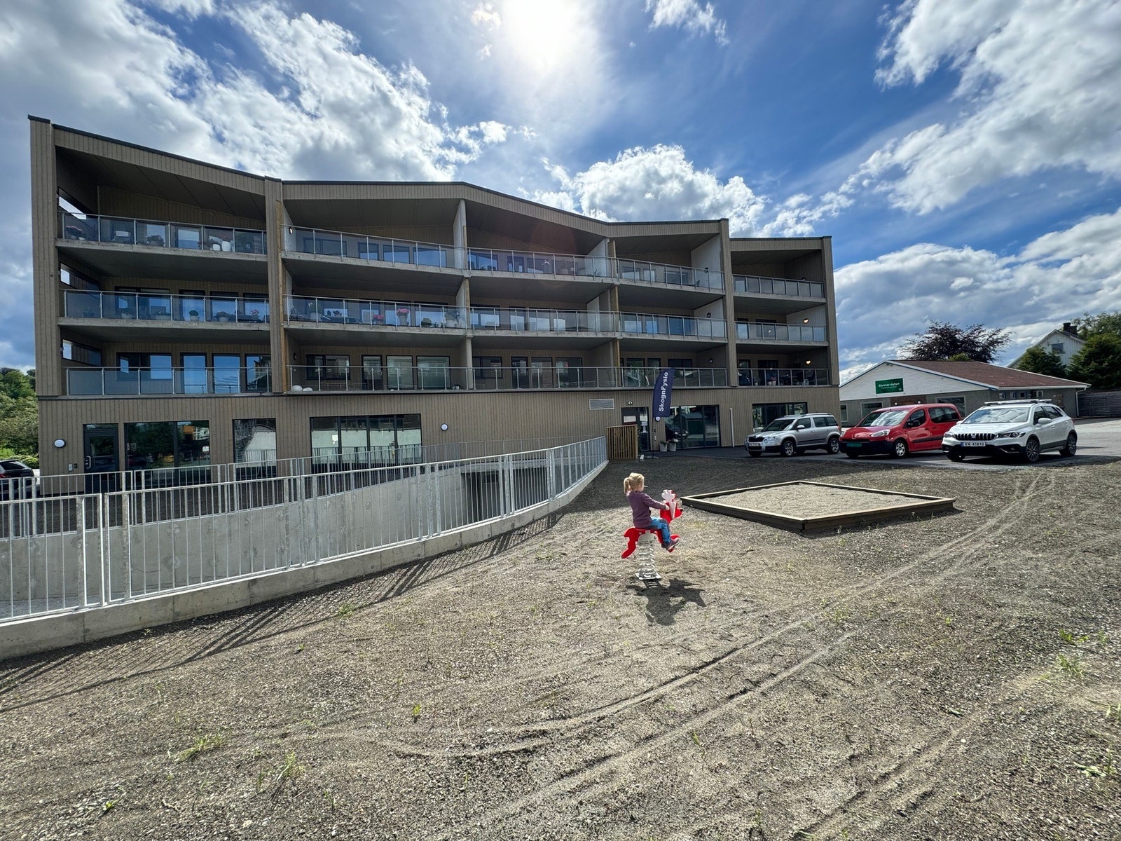 Pent opparbeidet uteområde utenfor bygget med plen og en liten lekeplass. Galleribilde