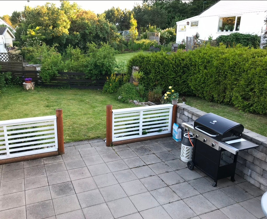 Del av terrasse og hage, mer terrasse (med levegg) og hage til venstre ut mot gjerde og lite trafikkert vei. Flere bilder kommer. Galleribilde