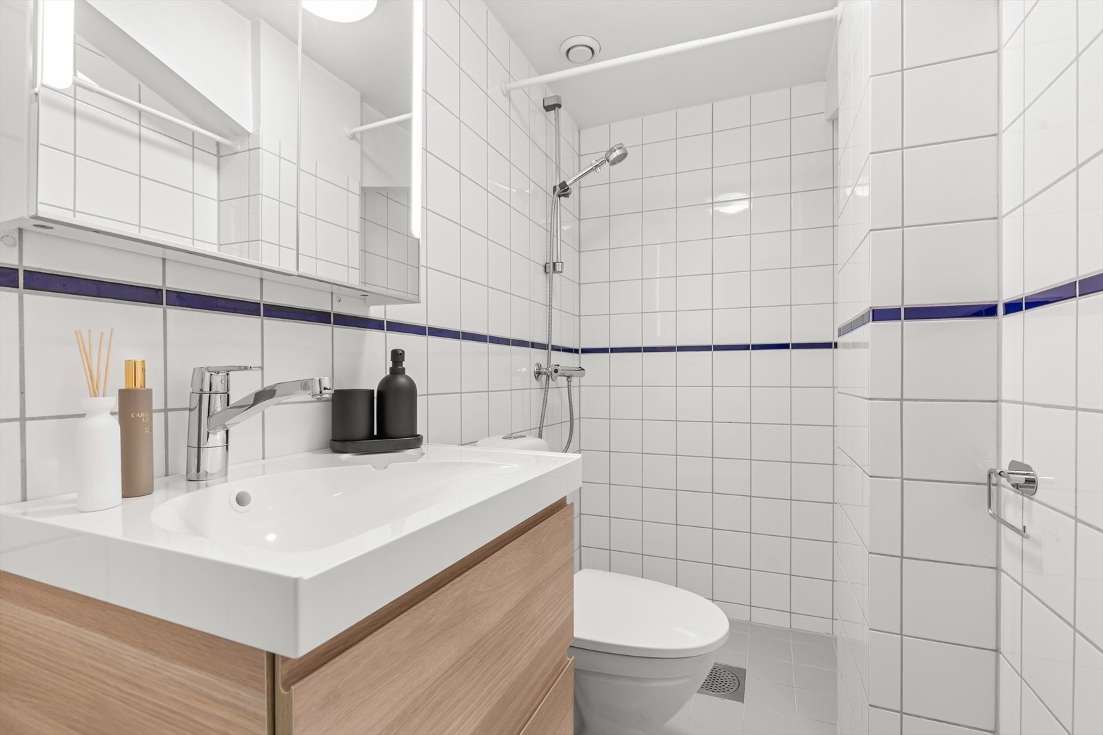 Lyst og pent flislaget baderom med stor dusjnisje, wc og baderomsinnredning med speilskap. Galleribilde