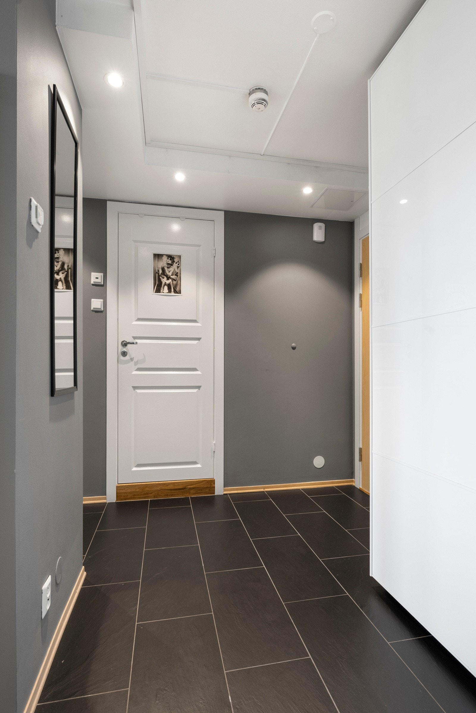 Entreen har gråmalte vegger og store, sorte gulvfliser Galleribilde