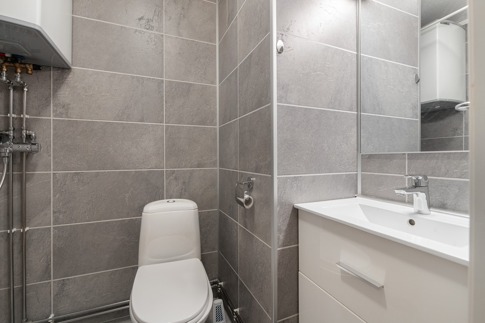 Pent bad som er overflateoppusset i nyere tid. Badet er utstyrt med gulvmontert toalett og åpen dusj, samt lys servantinnredning. Galleribilde