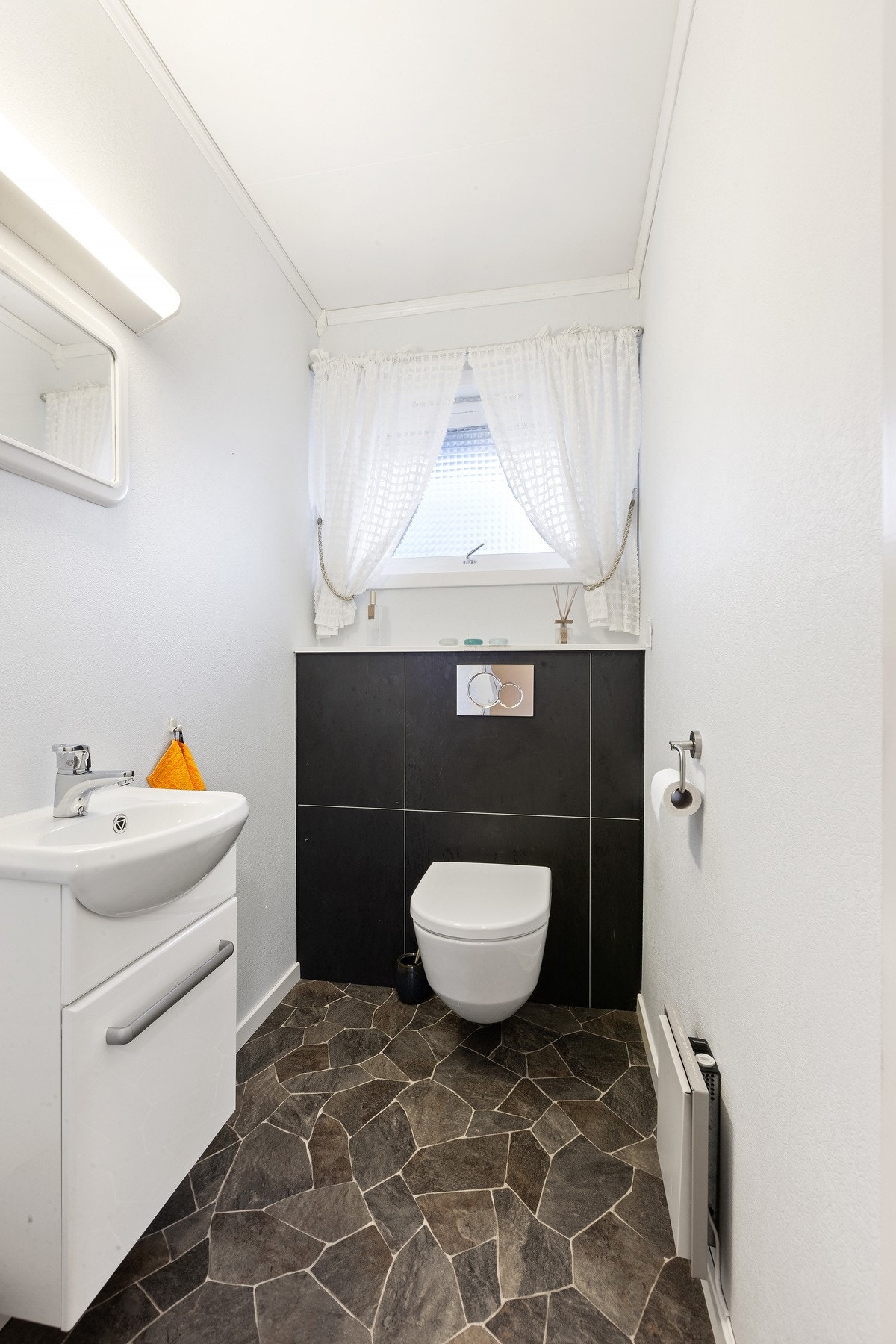 Toalettrom med veggehengt toalett samt servant med skuff under. Galleribilde