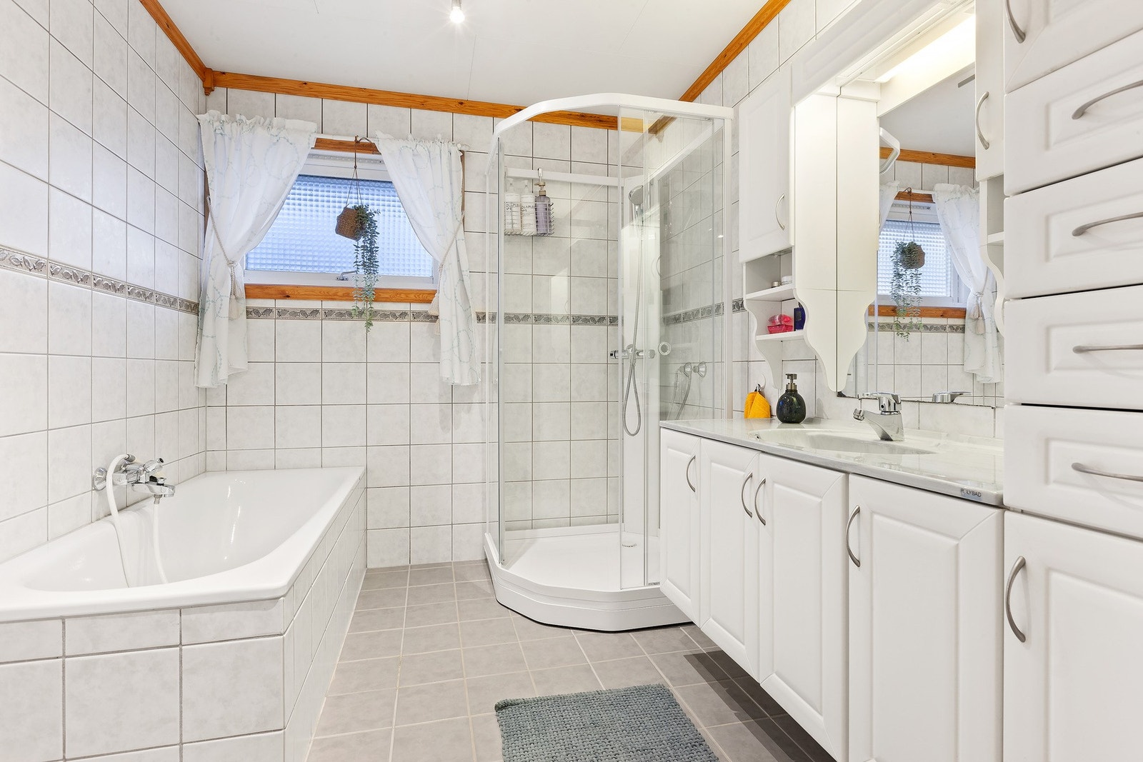 Lys innredning med nedfelt servant og skap under, overskap og speil med lys over, skuffeseksjon, badekar og dusjkabinett. Varme i gulv gir en lun og fin start på dagen. Galleribilde