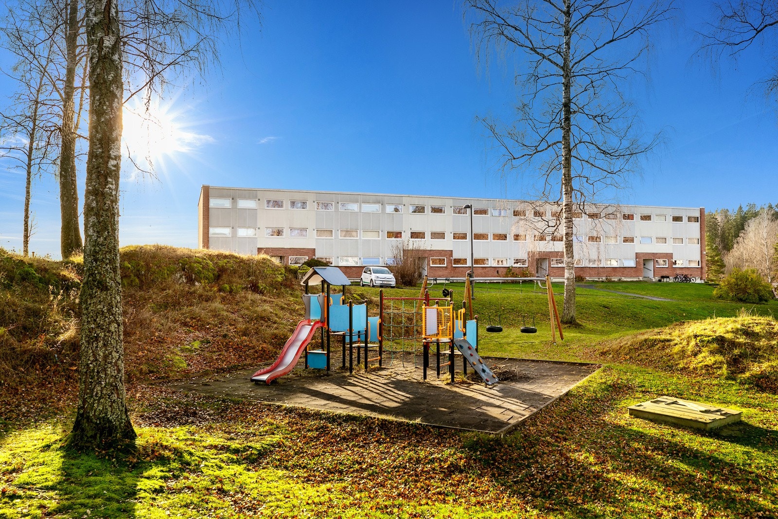 Fellesareal med asfalterte gangveier, lekearealer, sittebenker og store grøntområder med plener og små skogholt. Galleribilde