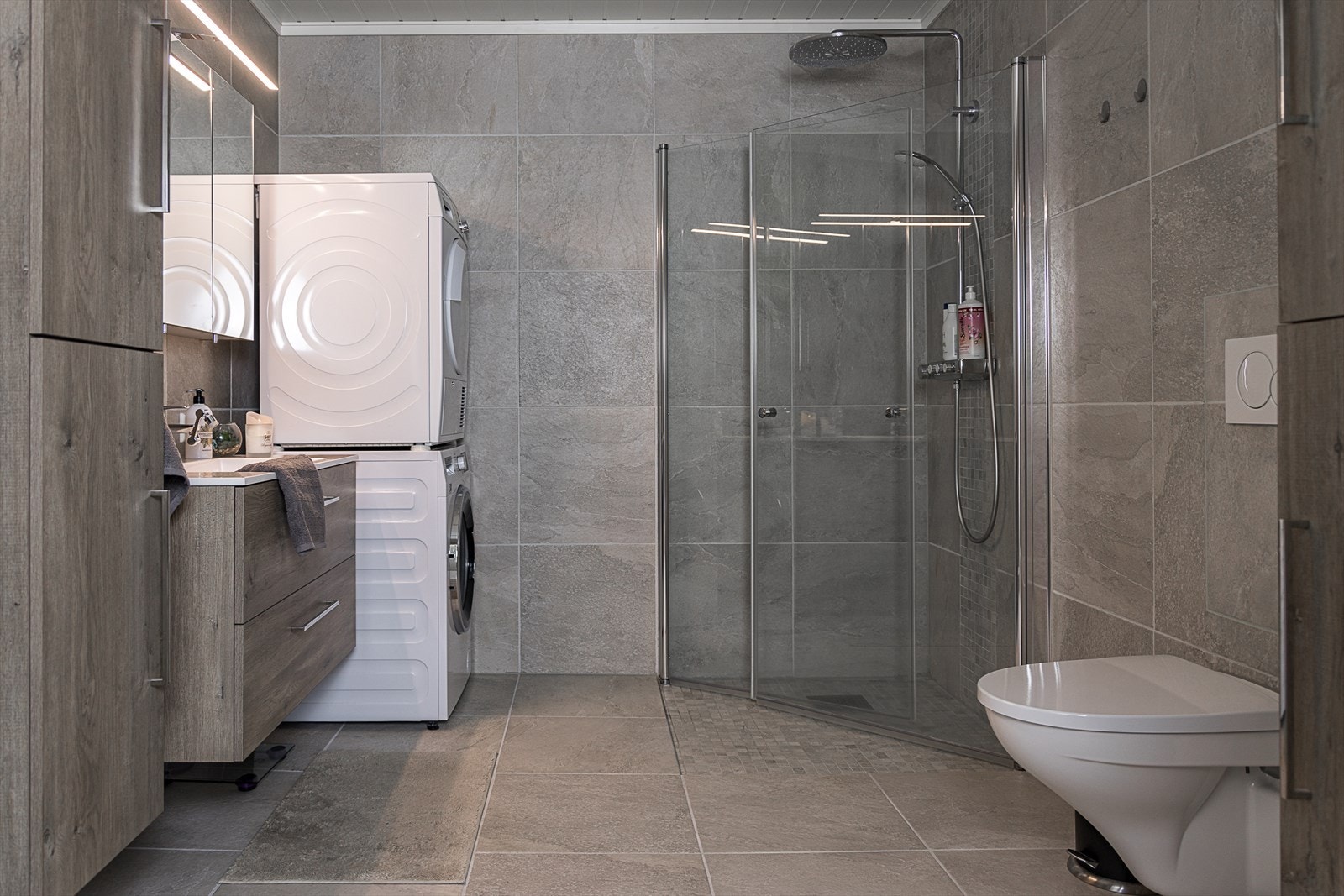 Badet har innredning med nedfelt servant, veggmontert toalett, dusjvegger/hjørne og opplegg for vaskemaskin. Galleribilde