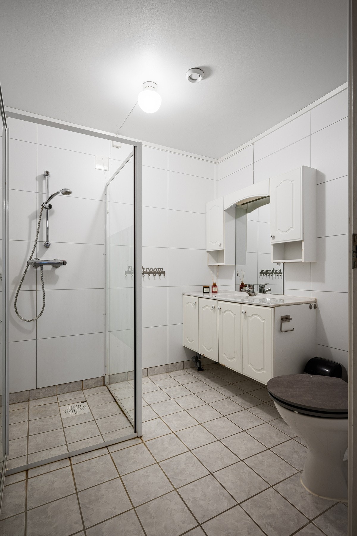 Bad i underetasje inneholder servantinnredning, toalett og dusjhjørne, og har flislagt gulv med varme Galleribilde