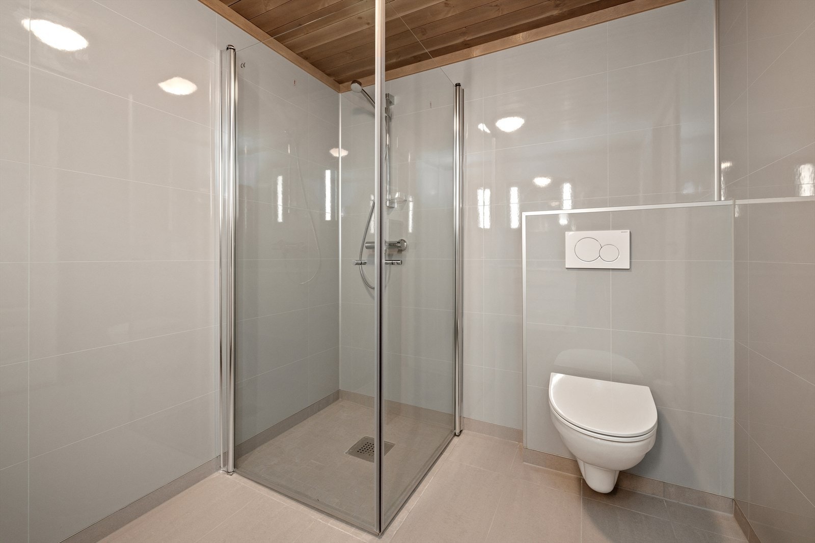 Badet er innredet med vegghengt toalett og dusjhjørne med foldedører i glass. Galleribilde