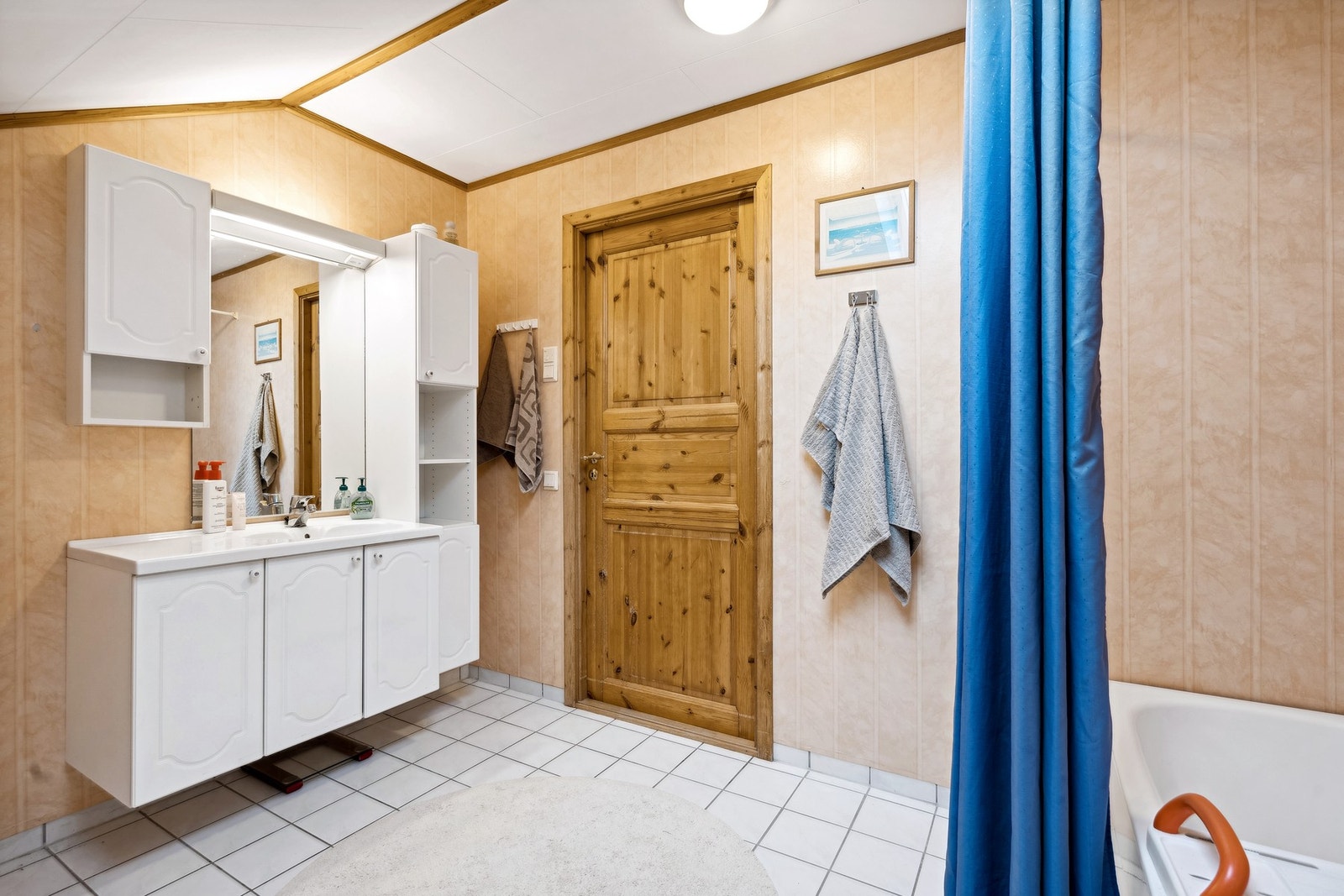 Baderommet har innredning med heldekkende servant, høyskap, overskap og speil med lys over Galleribilde