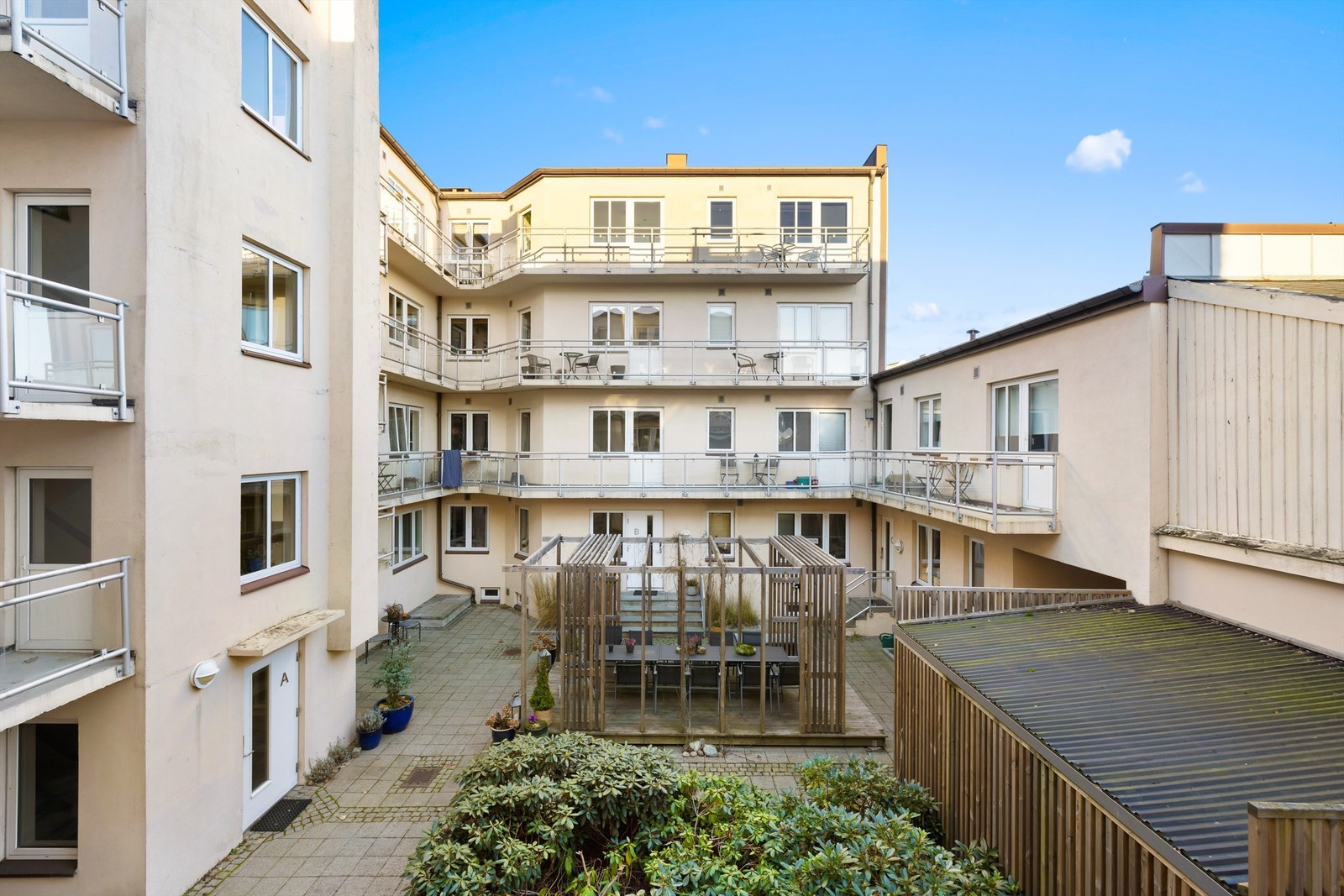 Utsyn fra balkongen mot borettslagets skjermede gårdsrom, med felles terrasse til bruk av beboerne. Galleribilde