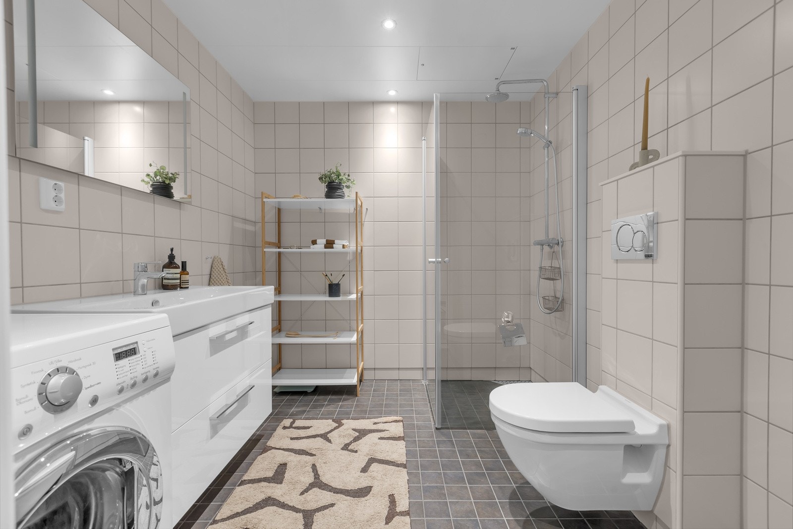 Pent og praktisk bad med fliser på gulv og vegger, innfellbare glassdører i dusjsonen og opplegg for vaskemaskin og tørketrommel Galleribilde