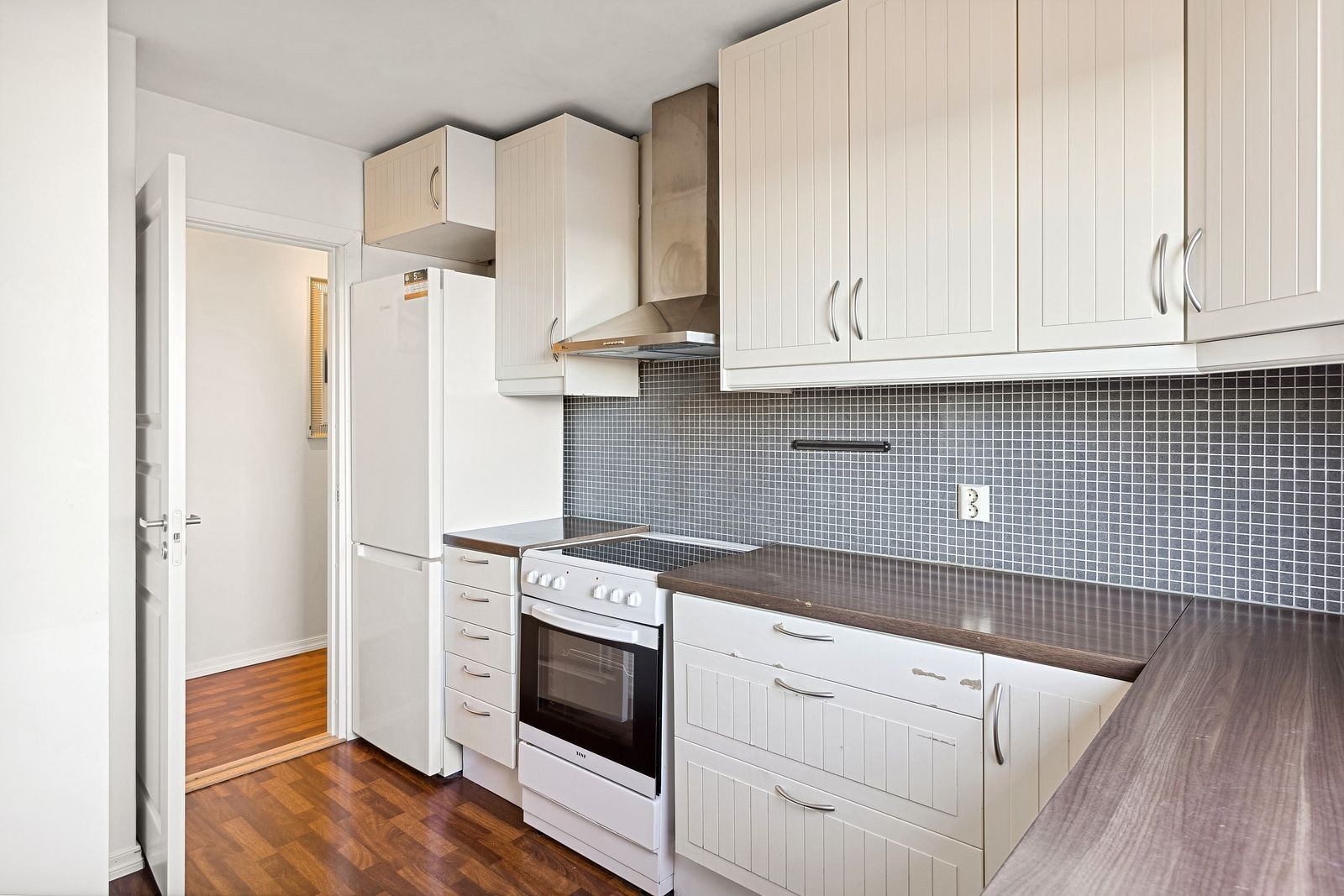 Lyst kjøkken med kjøleskap komfyr. Opplegg for vaskemaskin på kjøkkenet. Galleribilde