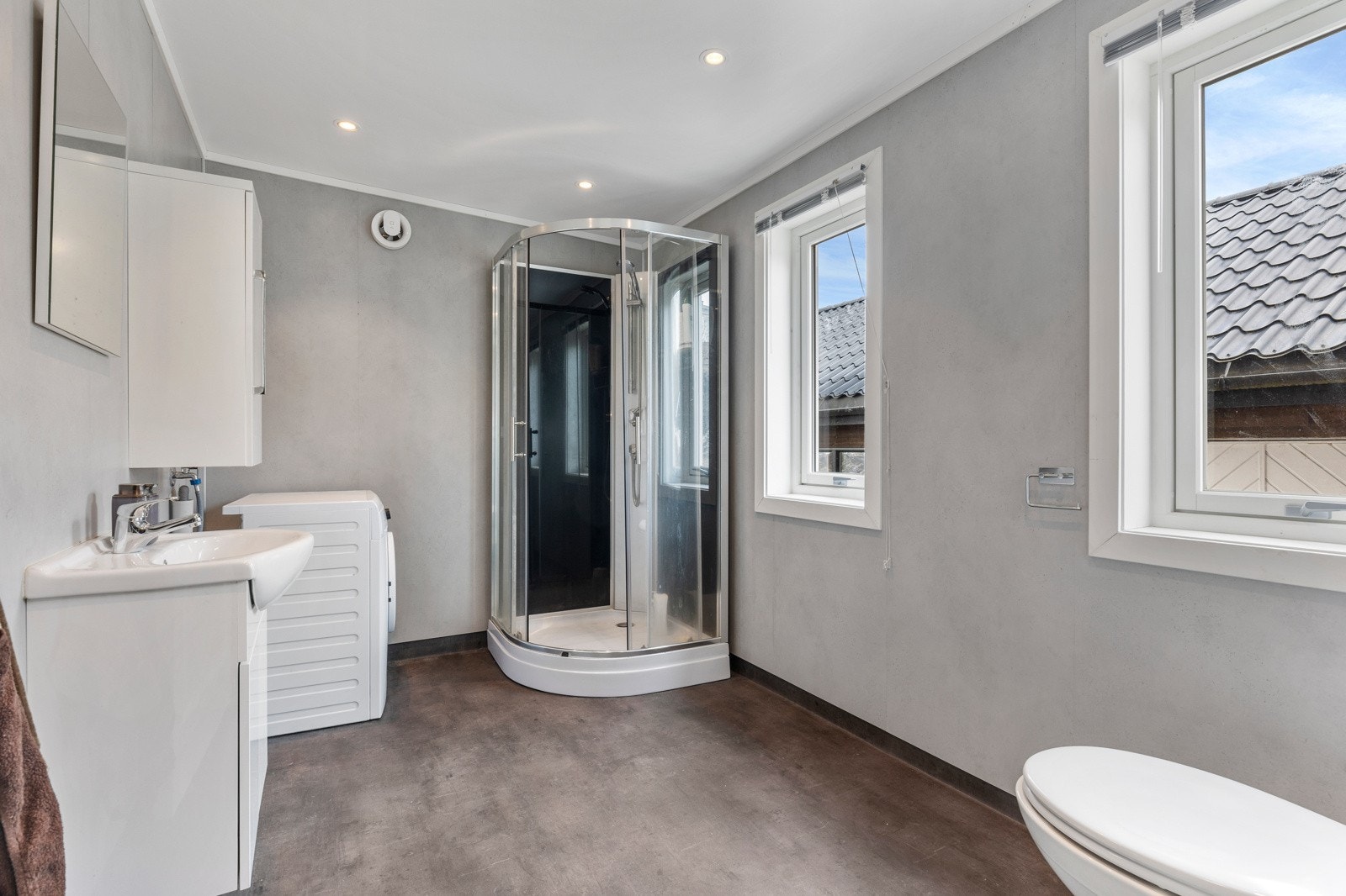 Baderom bestående av servant med underskap, dusjkabinett, toalett og opplegg for vaskemaskin Galleribilde