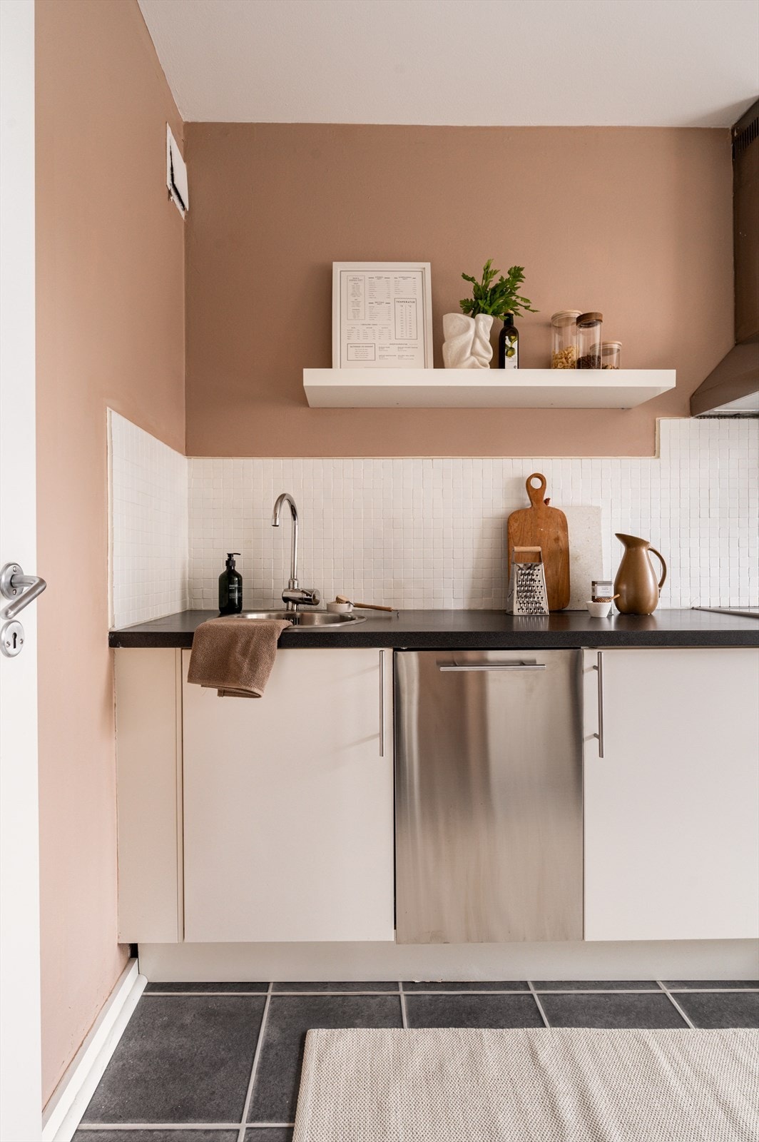 Kjøkkeninnredning med glatte fronter, laminat benkeplate med nedfelt vaskekum. Fliser over benkeplate, kullfilter over kokeplass., samt opplegg for oppvaskmaskin. Galleribilde