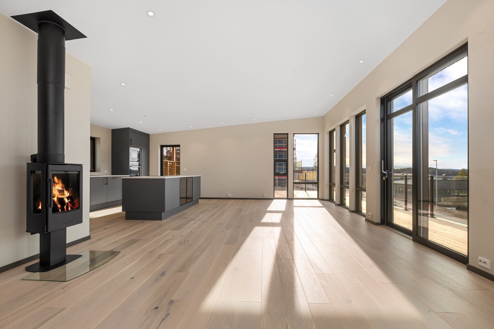 romslig stue og kjøkken på nesten 60 kvm med enstavs eikeparkett på gulv og malt gips på vegger. LED downlights i tak. Store vinduer med fin utsikt mot horisonten. Stålpipe med vedovn type Hvam Wiking Galleribilde