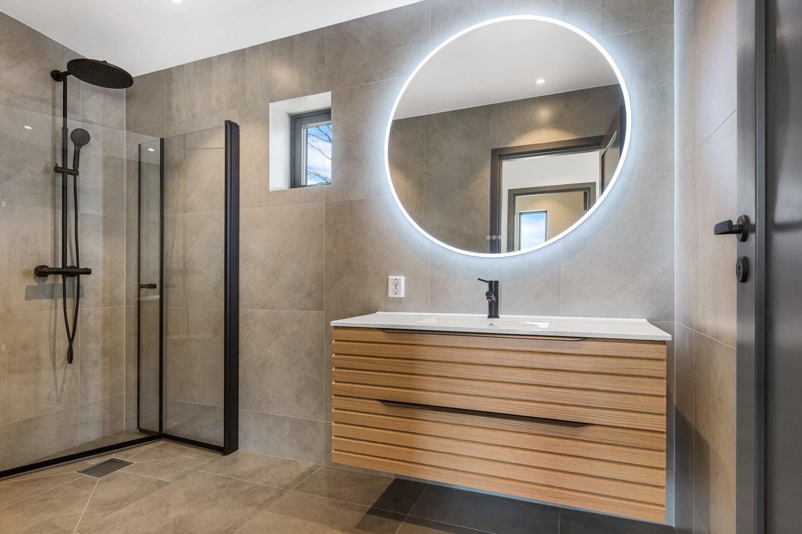 Bad/wc i 1. etasjen med fliser på gulv og flislagte vegger. Veggmontert wc. Dusjvegger med glassdører. Baderomsinnredning fra Viking bad. Speil med dimmbart LED lys og 3 fargevalg med memory Galleribilde