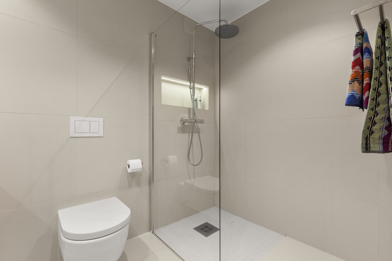 Badet inneholder servantinnredning med helstøpt servant, speilskap, vegghengt toalett og dusjhjørne. Opplegg for vaskemaskin under benkeplaten. Galleribilde