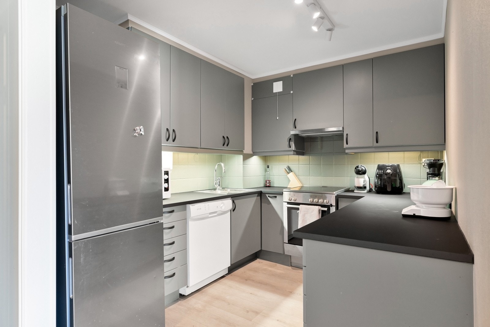 Moderne kjøkken som består av glatte fronter og benkeplate i lamiant. Galleribilde