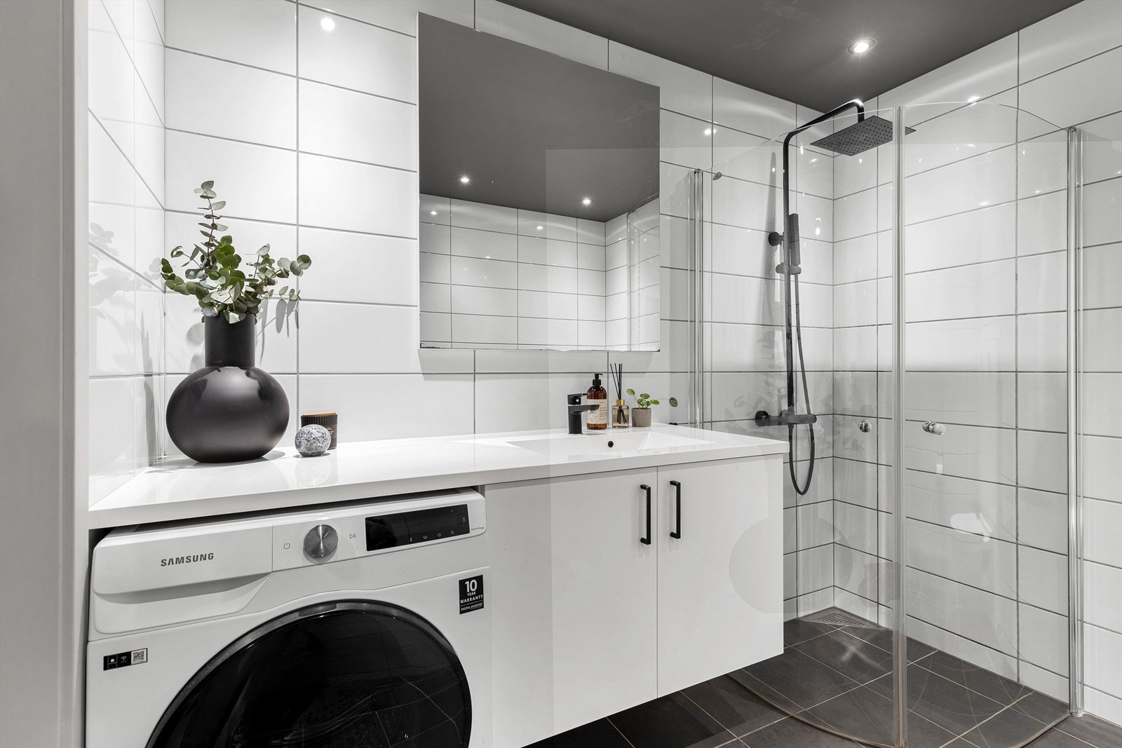 Badet er innredet med dusj med dører i herdet glass, veggfestet klosett, benk med servant og skap for oppbevaring. Galleribilde