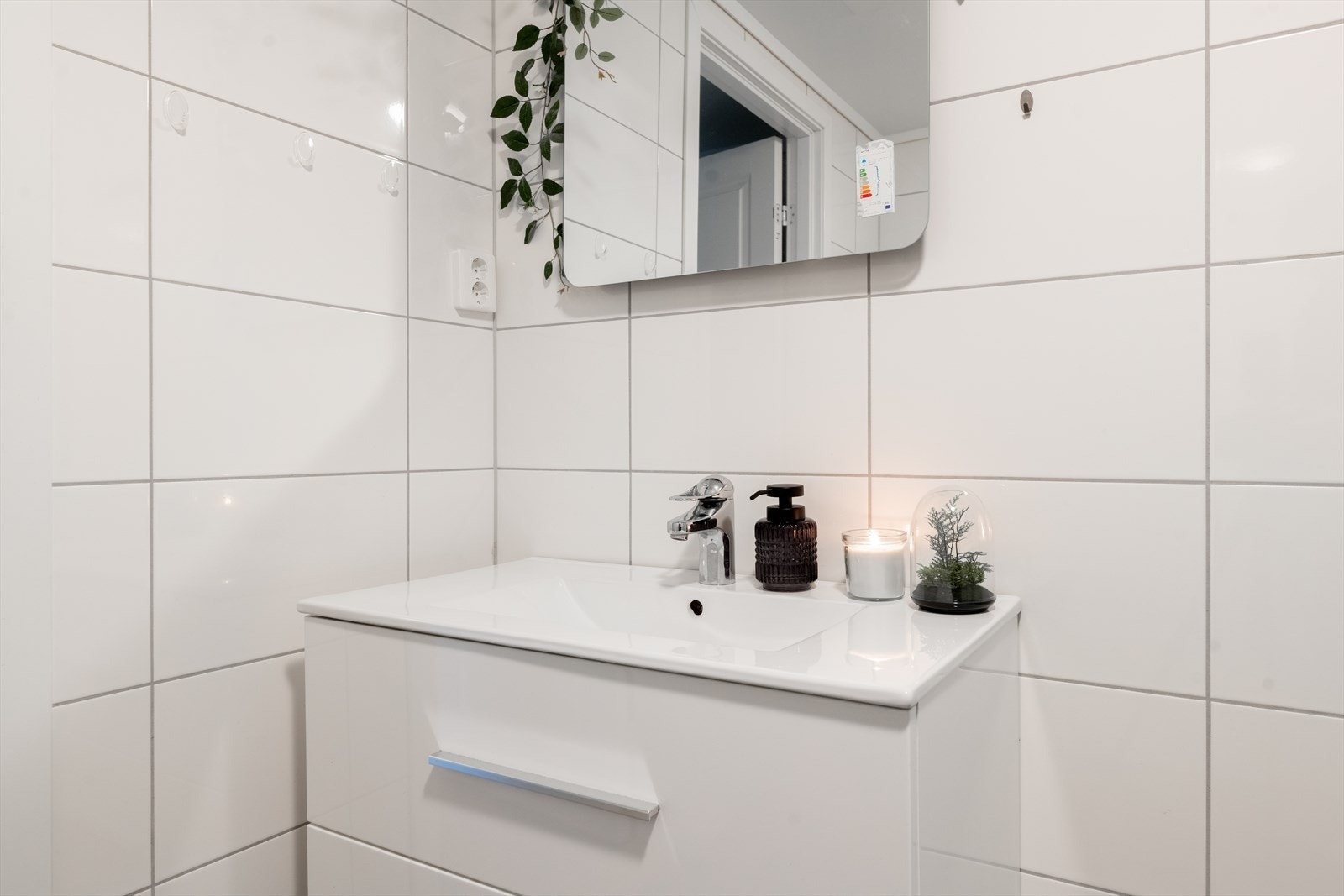 Badet har hvit innredning med dype skuffer og heldekkende servant, samt dusjkabinett og veggmontert toalett. Galleribilde