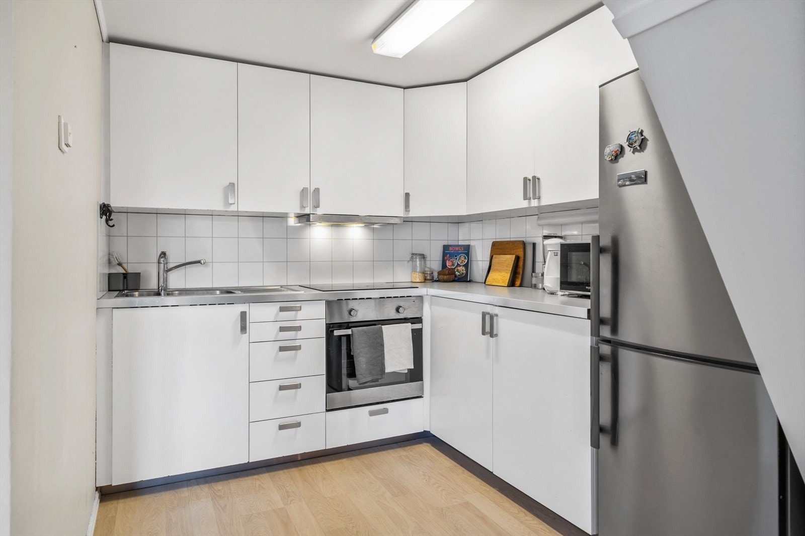 Stilrent kjøkken med hvite overflater og laminat benkeplate, samt fliser på vegg Galleribilde