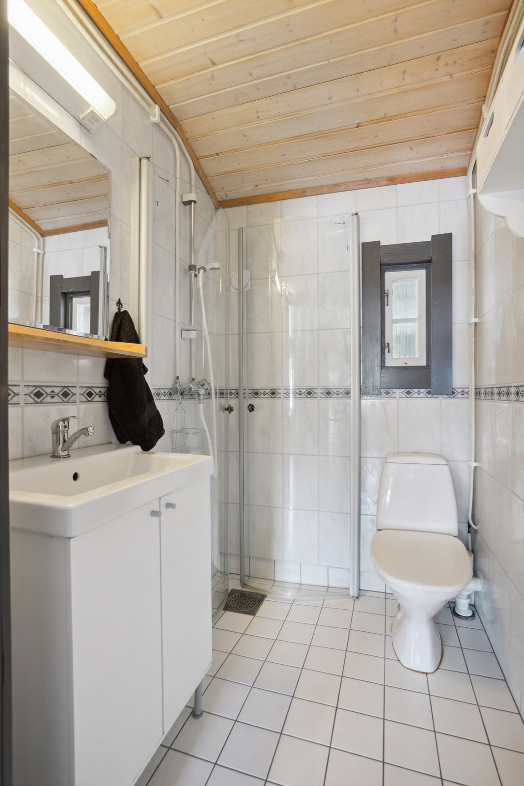 Badet har flislagt gulv, hvit innredning, wc og dusjnisje Galleribilde