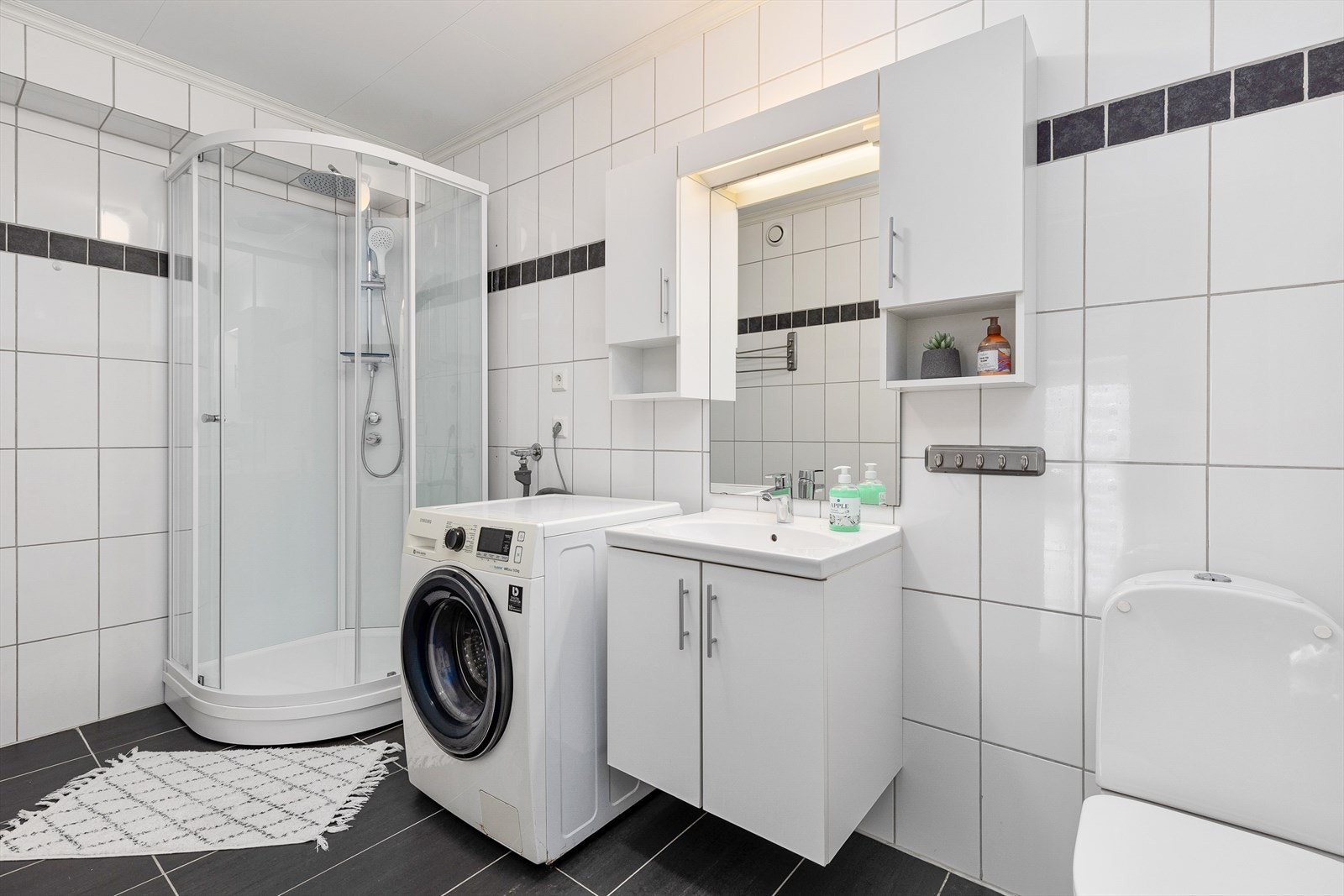 Badet er flislagt og utstyrt med innleiing med servant, dusjkabinett, opplegg for vaskemaskin og toalett. Galleribilde