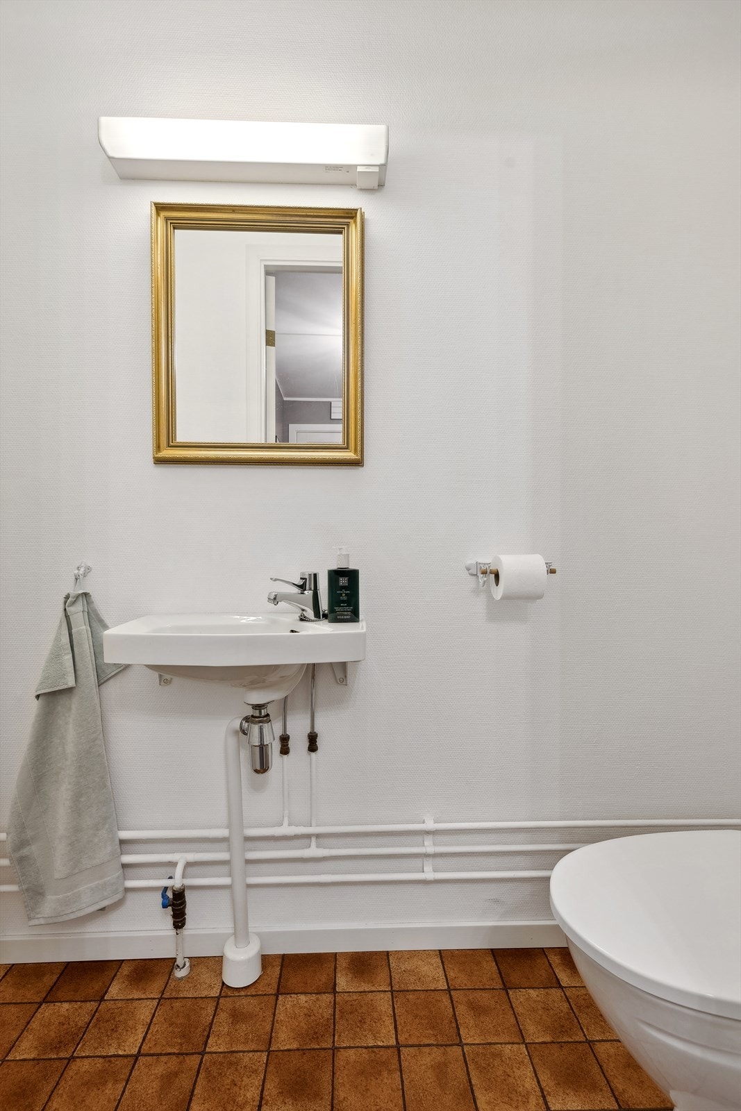 Separat WC innredet med vegghengt servant med ett-greps blandebatteri, gulvstående toalett og lysarmatur. Galleribilde
