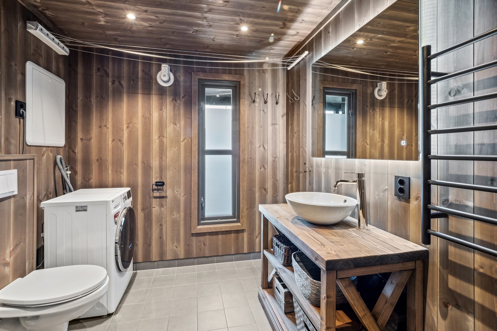 Baderommet har brunbeiset panel på veggene, grå fliser på veggene i dusjsonen og grå fliser på gulvet. Galleribilde