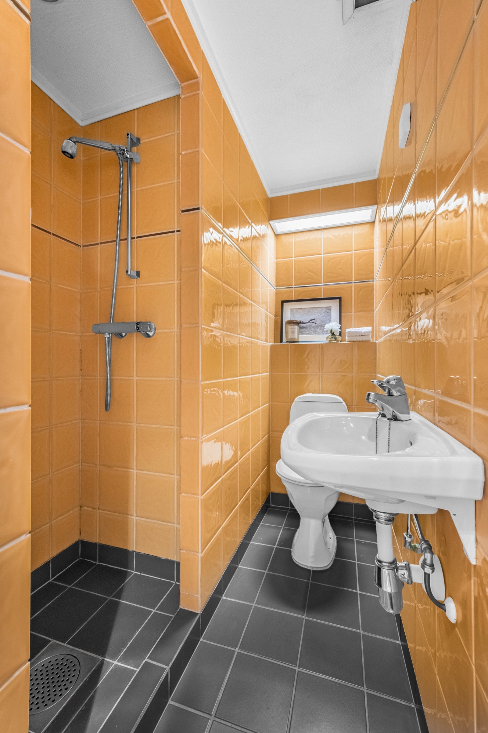 Badet er helfliset og utstyrt med varmekabler, som gir en behagelig varme. Veggene har oransje fliser med innkassinger, mens gulvet er dekket av mørke fliser i størrelse 20x20 cm Galleribilde