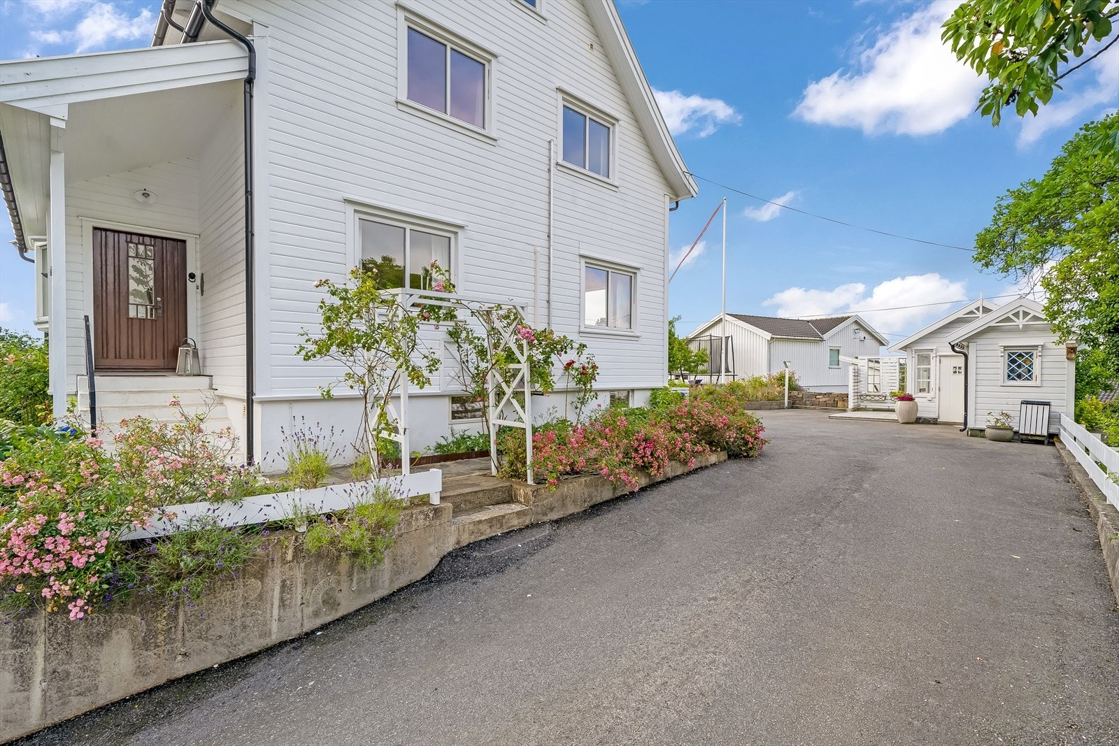 Pent opparbeidet uteområde med beplantede bed, plenlagte området og asfaltert innkjørsel/tun. Galleribilde