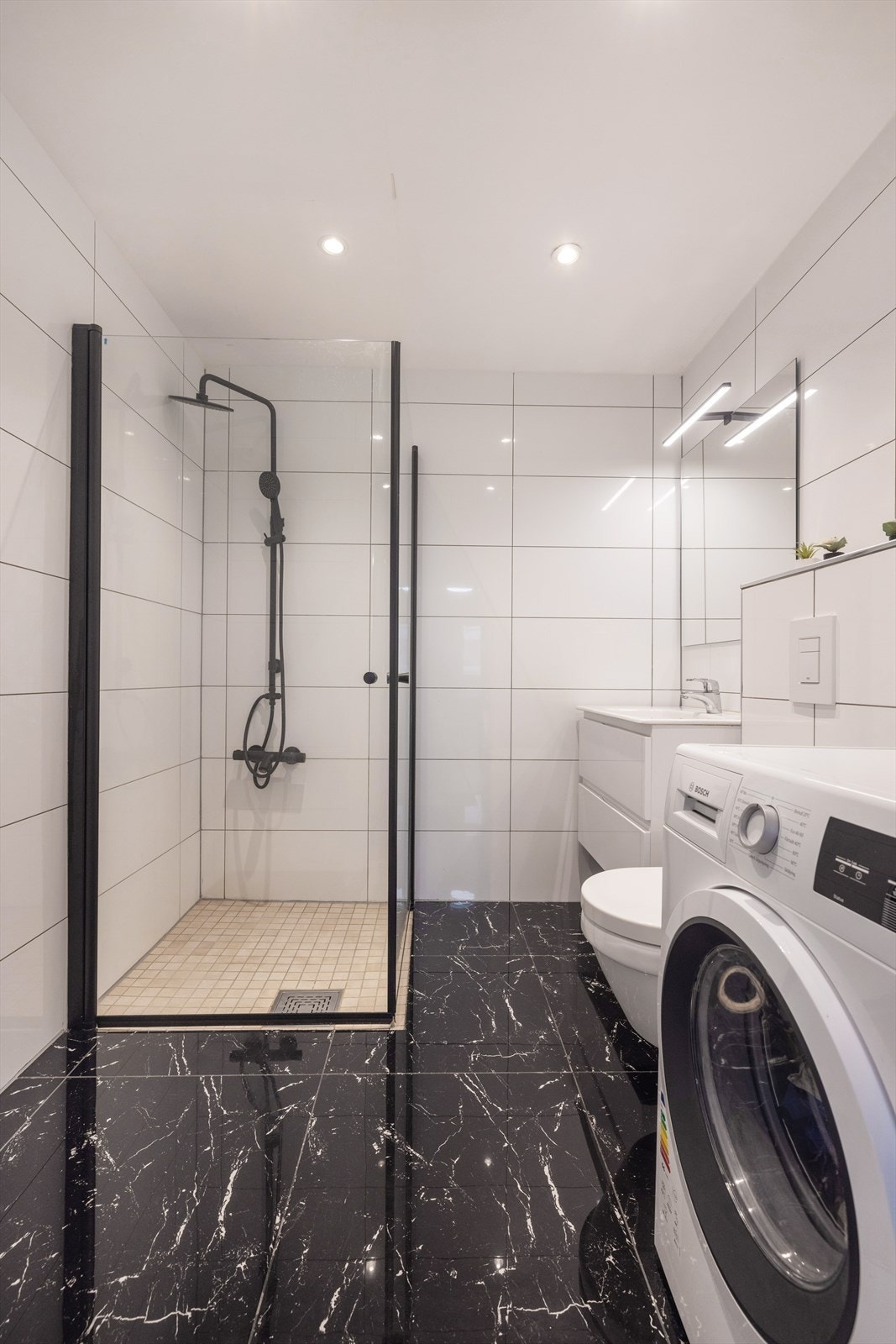 Badet inneholder vegghengt toalett, dusjhjørnet med innfellbare glassvegger, servant med skuffer og opplegg til vaskemaskin. Galleribilde