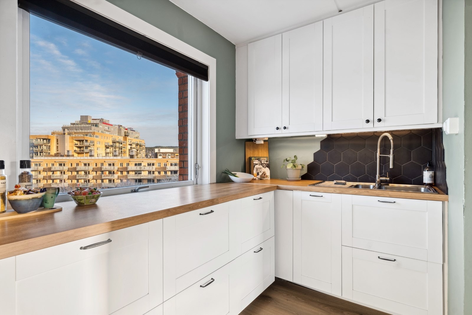 Kjøkkeninnredning med hvite profilerte fronter, laminat benkeplate, 1 1/2 oppvaskkum i stål med avrenningsfelt og fliser over benk. Galleribilde